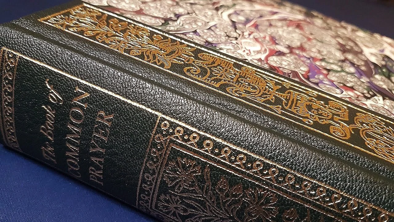 Close-up of an ornate, vintage-looking book with a black leather cover and gold embossed decorative patterns and text.