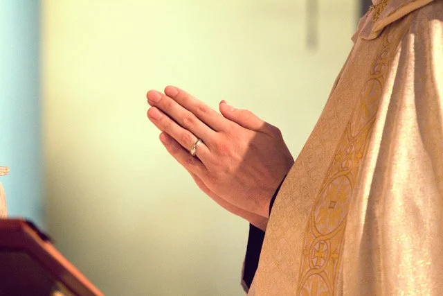 Person praying with hands clasped together, wearing a religious robe.