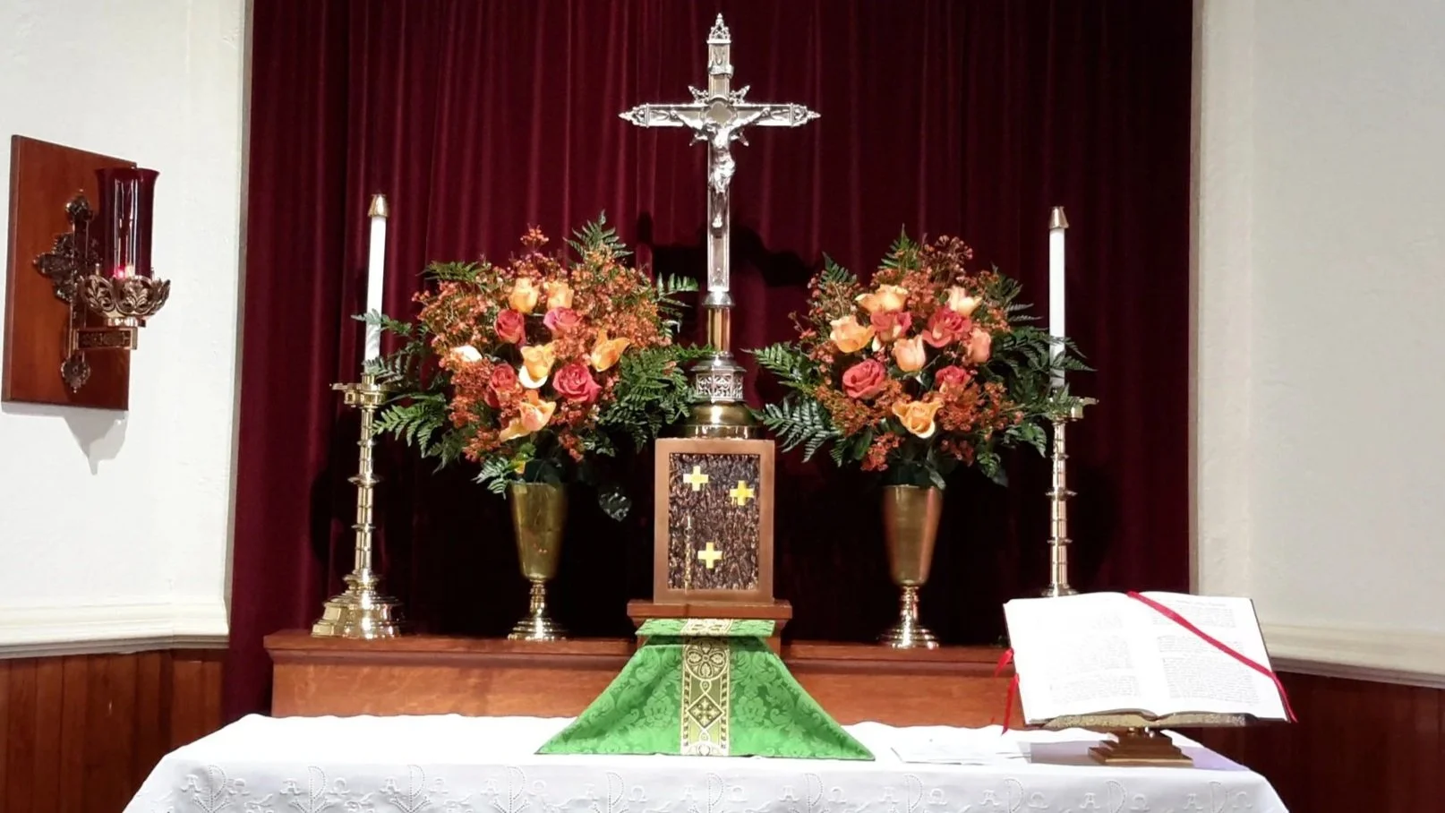 A wooden confessional booth in a church with Christian symbols, flanked by yellow and orange roses.