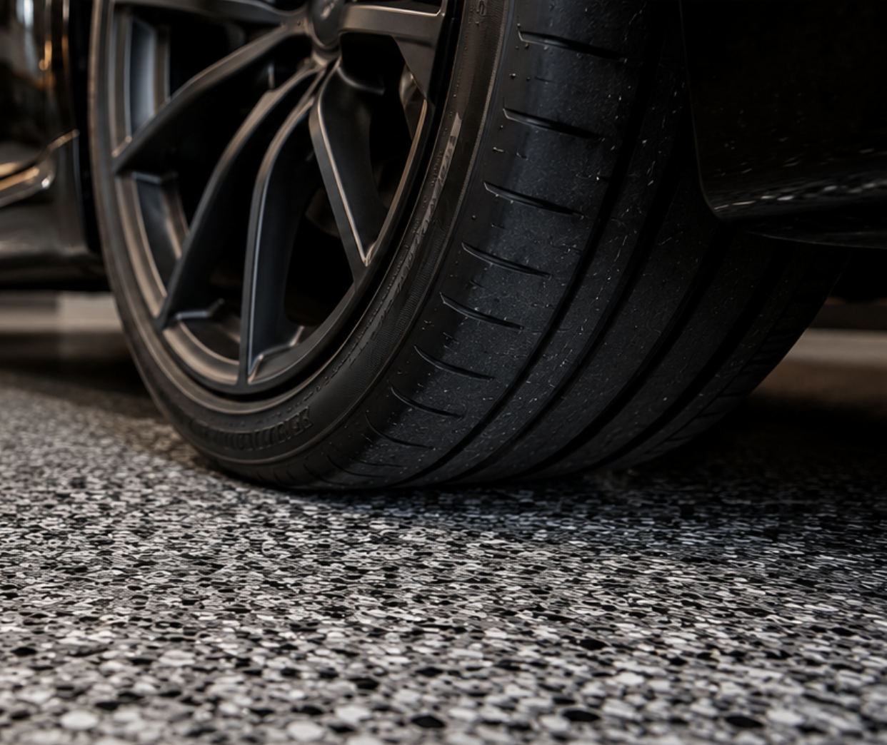 Close-up of a car tire and wheel on a textured grey surface.