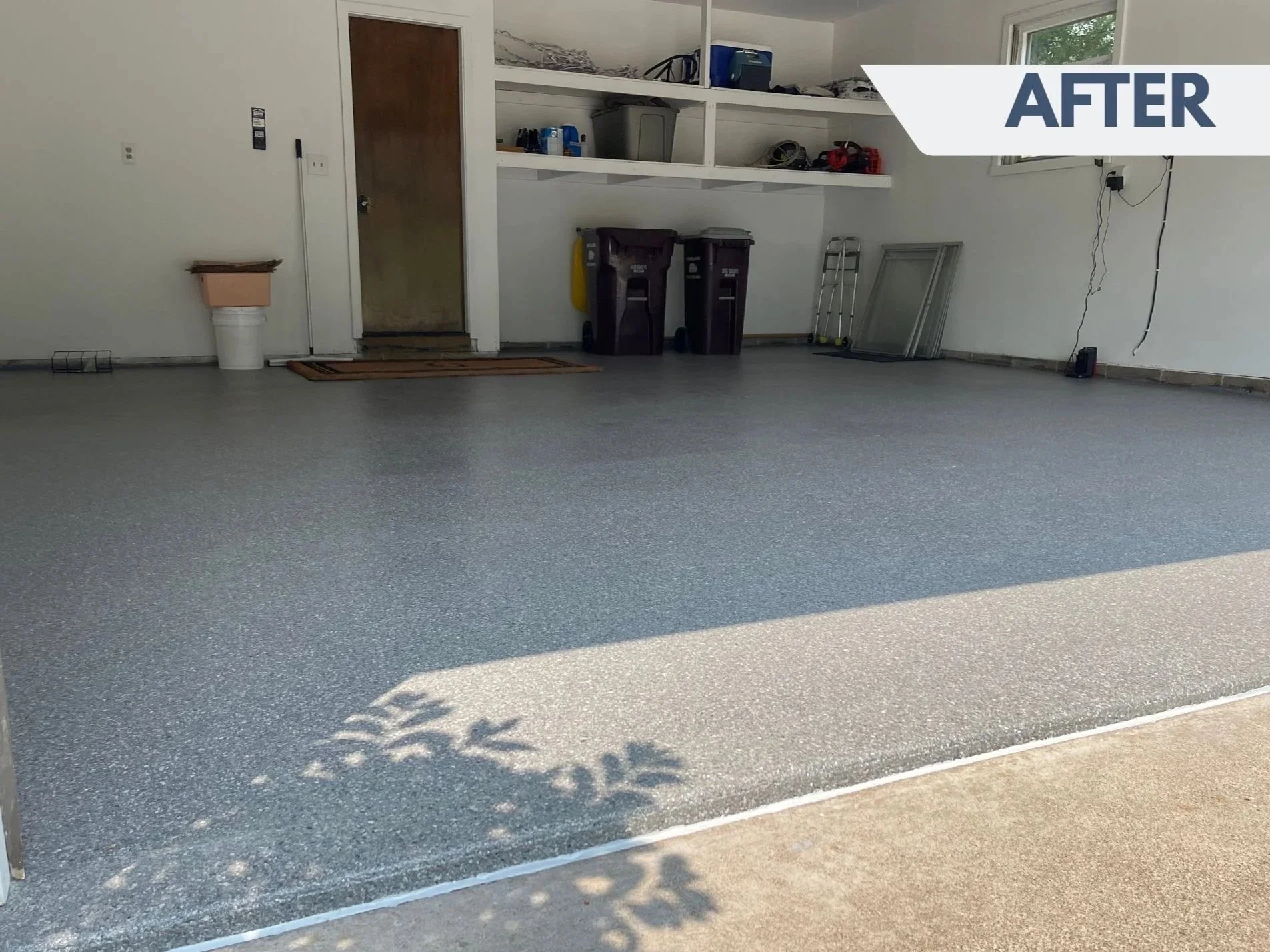 Clean garage with gray epoxy floor, shelves with storage items, and sunlight casting shadows on the floor.