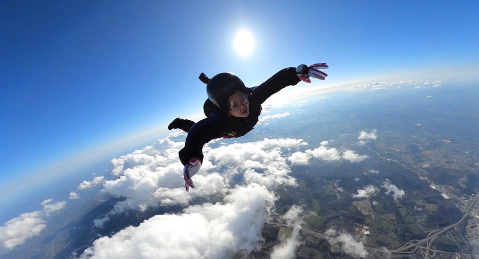 Person skydiving in mid-air above clouds and landscape.