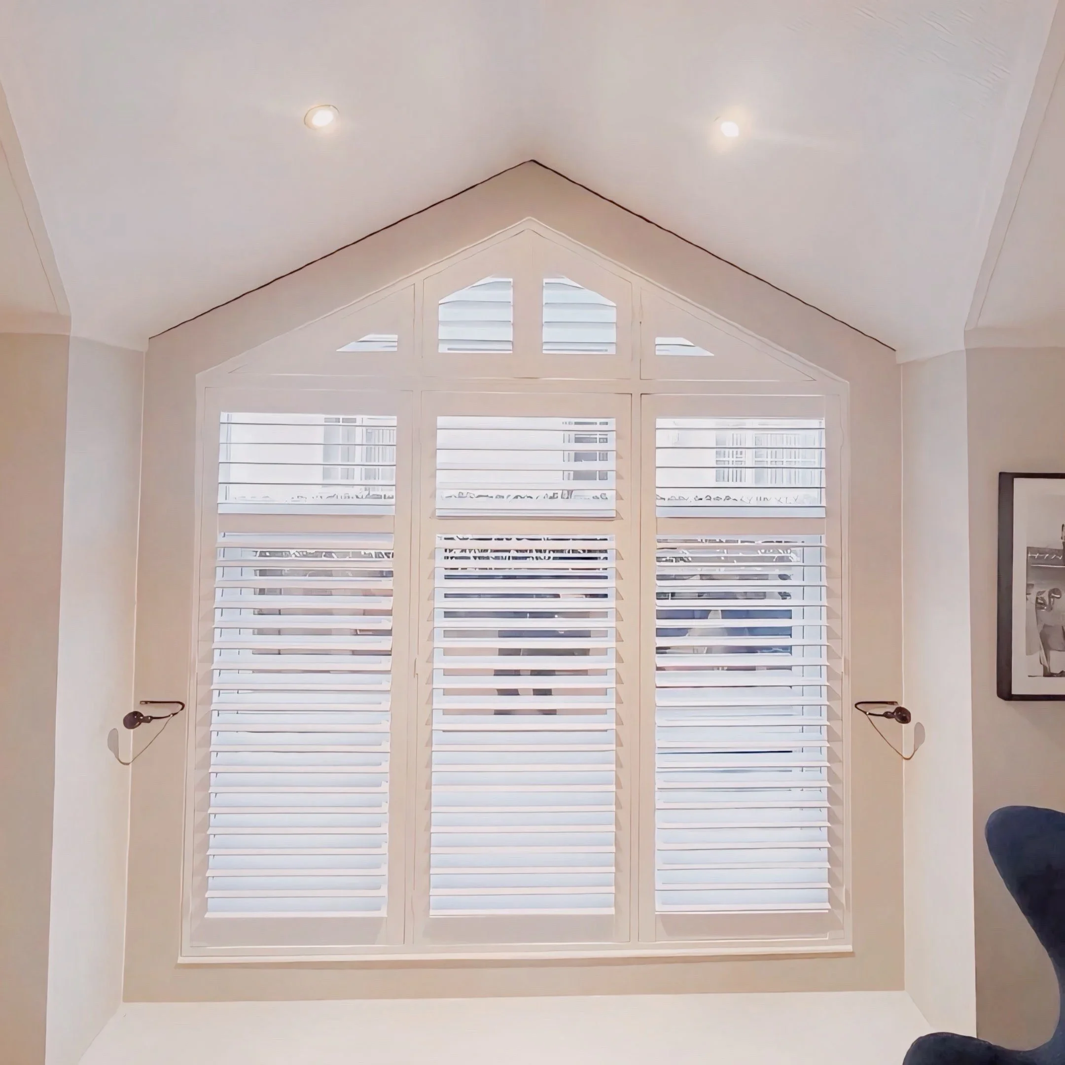 Ceiling with recessed lighting and large windows with white shutters in a room.