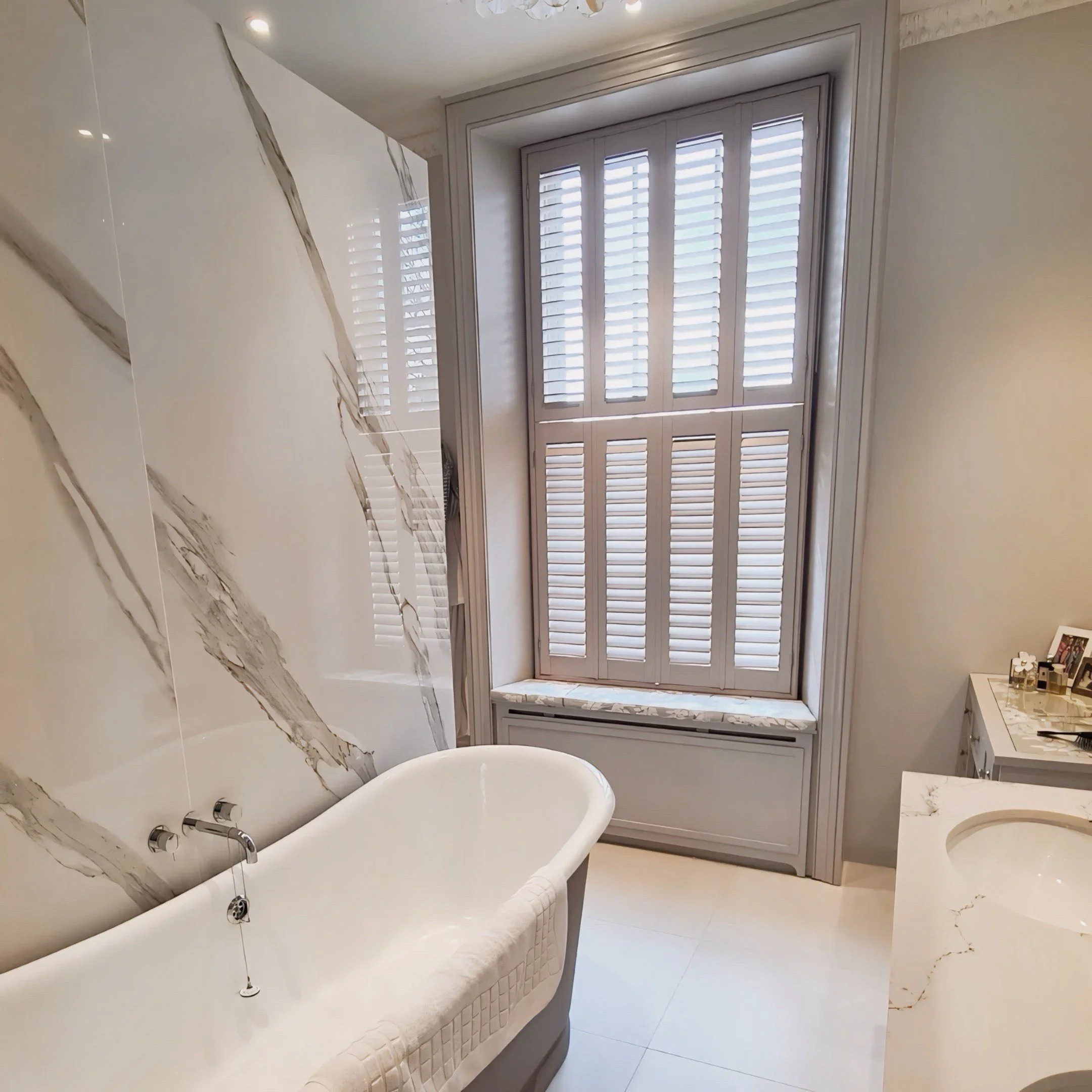 A bathroom with a white bathtub, marble walls, and a window with closed white shutters.