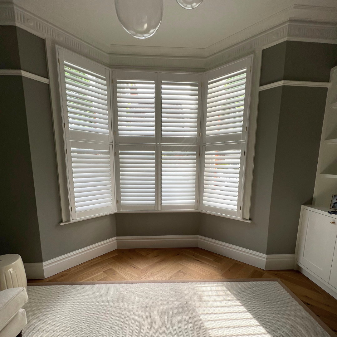Room with large bay window with white shutters, hardwood floor, and built-in white cabinet in the corner.