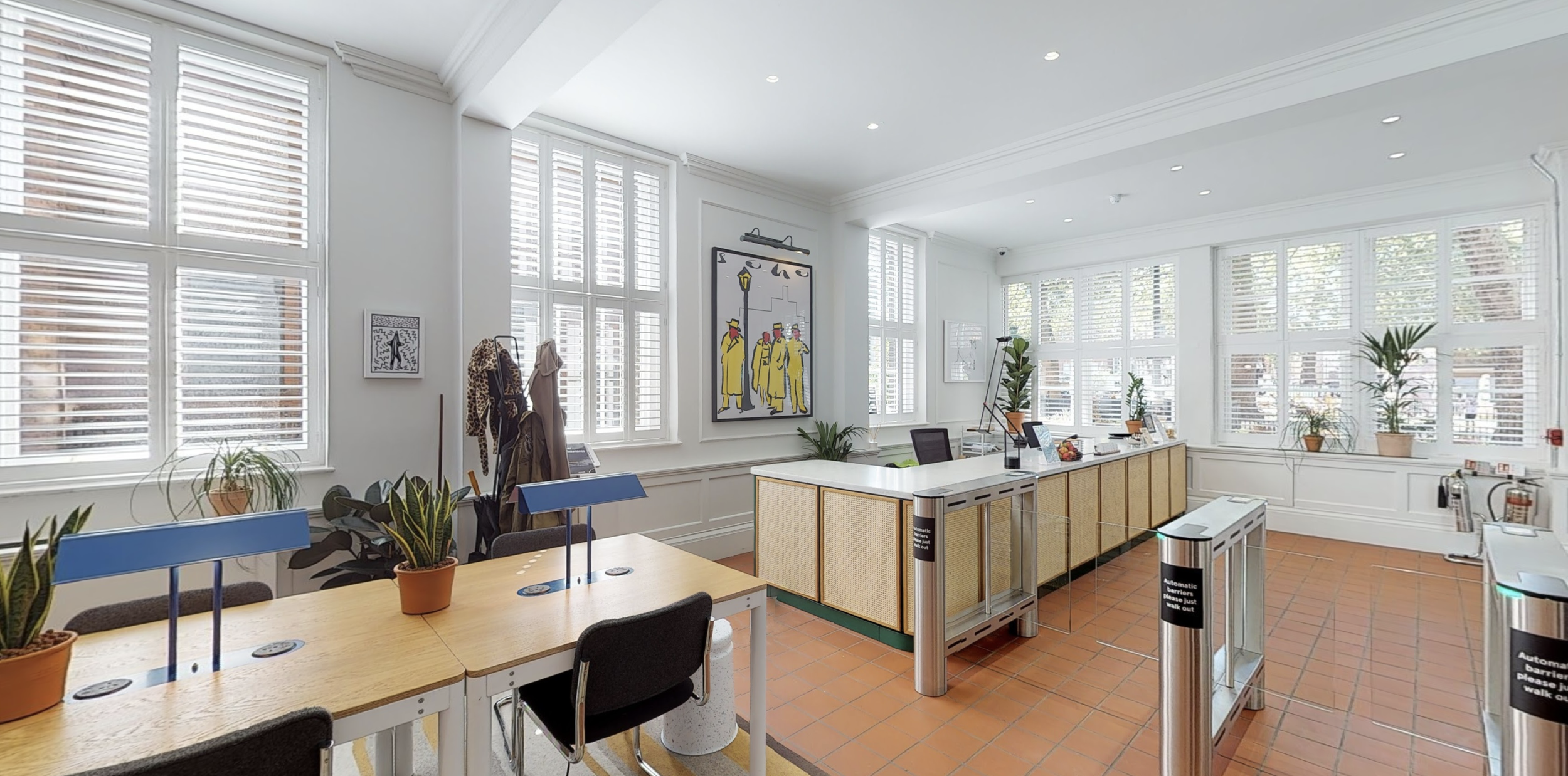 Bright indoor space with large windows, potted plants, and modern decor, including artwork and a coat rack.