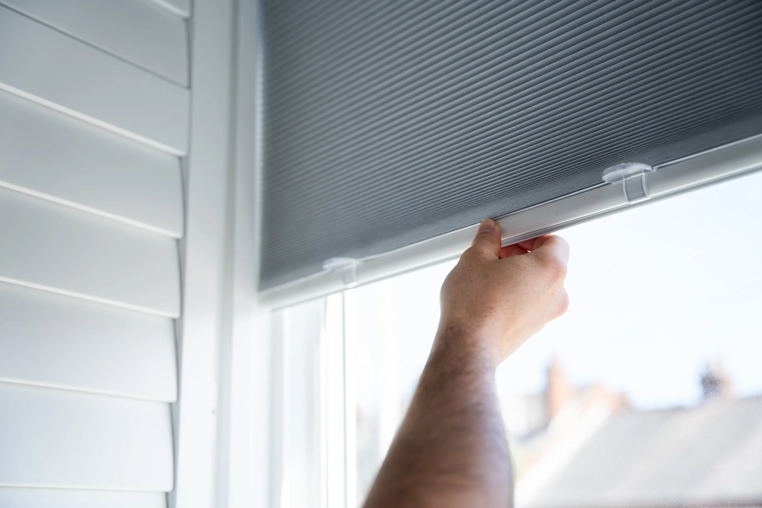 A person installing or adjusting a window screen on a white building, with the person's hand lifting the screen frame.