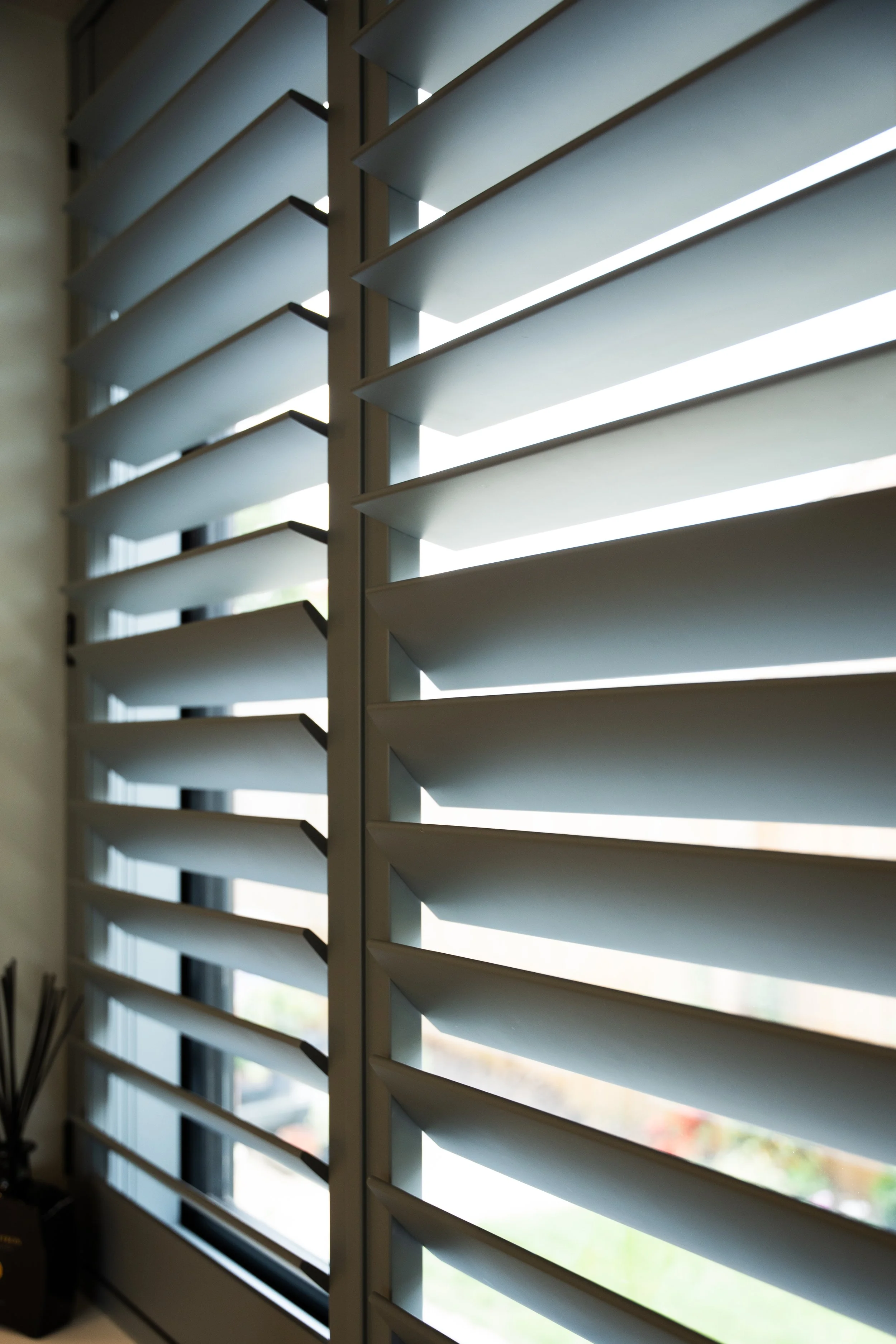 Close-up of window shutters with sunlight filtering through, revealing a glimpse of the outdoors.