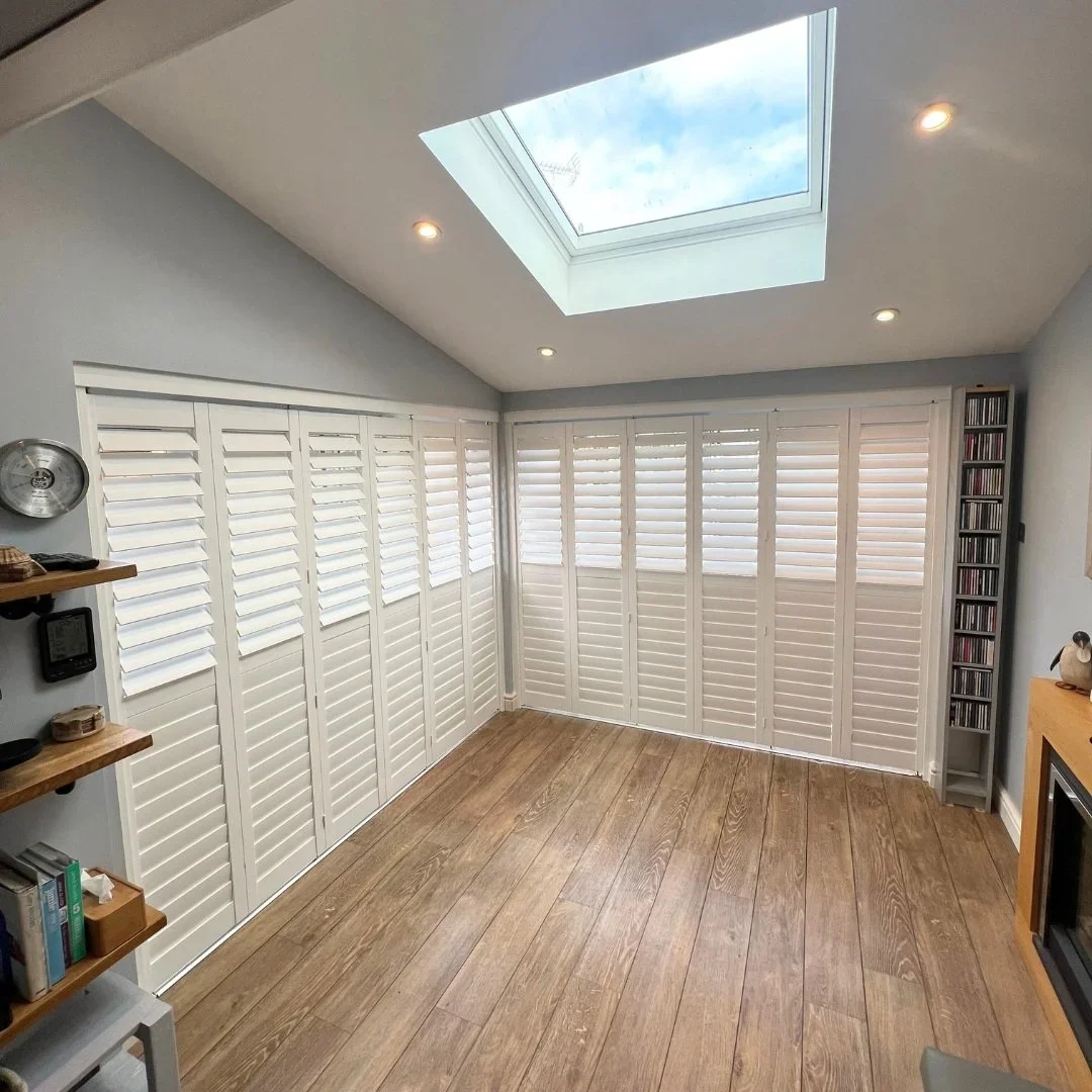 Room with wooden floor, white plantation shutters, ceiling skylight showing clouds and blue sky, and recessed lighting.