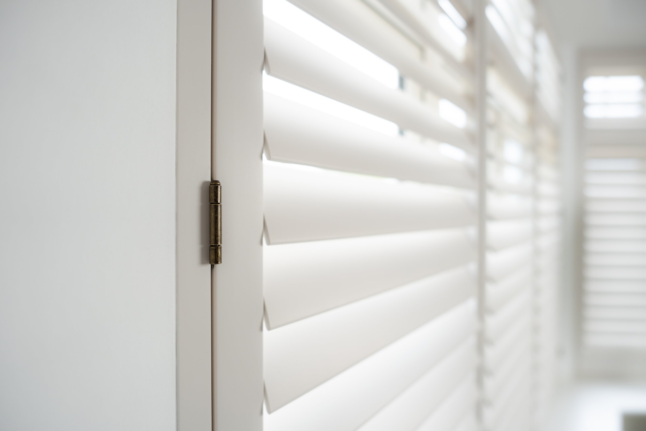 Close-up of white window shutter blinds, showing metal hinges and slats.