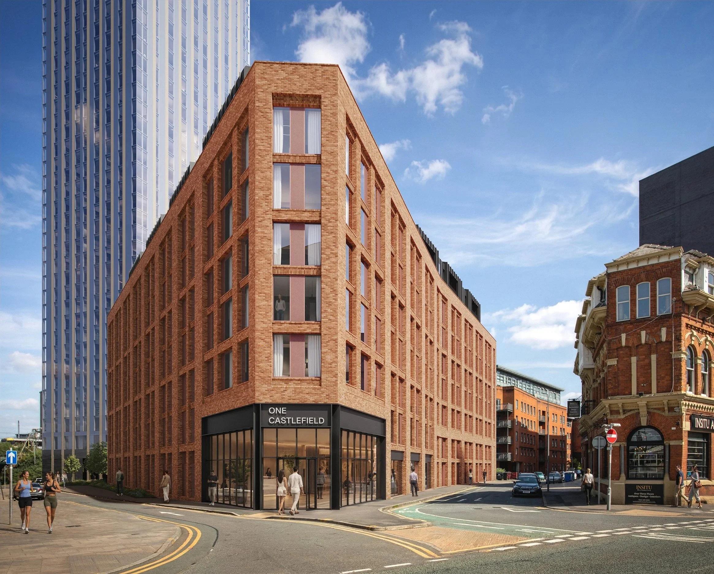 A modern red brick building with large windows, labeled "ONE CASTLEFIELD" at street level, situated in an urban area under a partly cloudy blue sky. People are walking on the sidewalk, and cars are on the street.