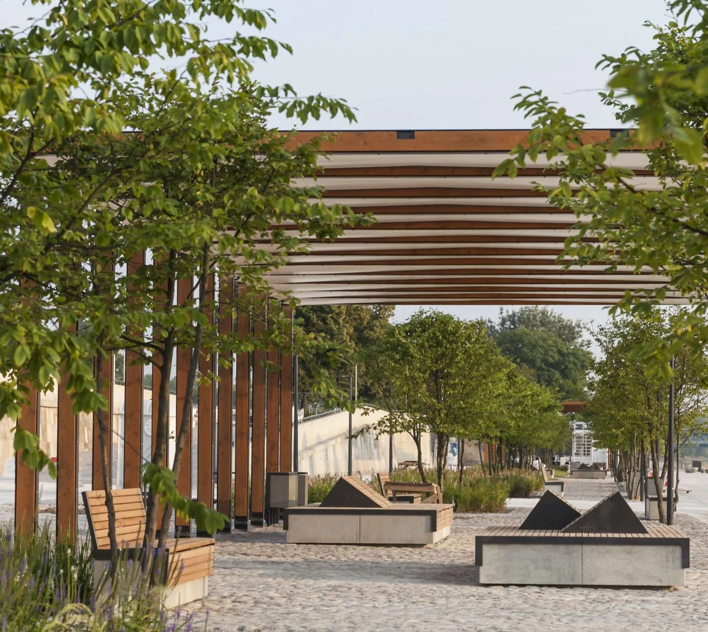 Public park with trees, benches, stone planters, and a wooden gazebo.