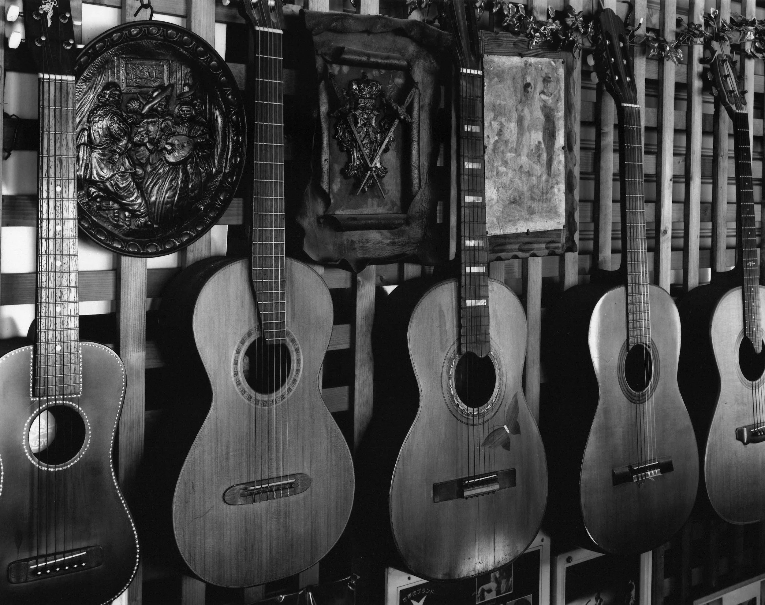 Multiple acoustic guitars hanging on a wall with wooden slats, along with carved wooden decorative plaques and a stone slab with relief carvings.