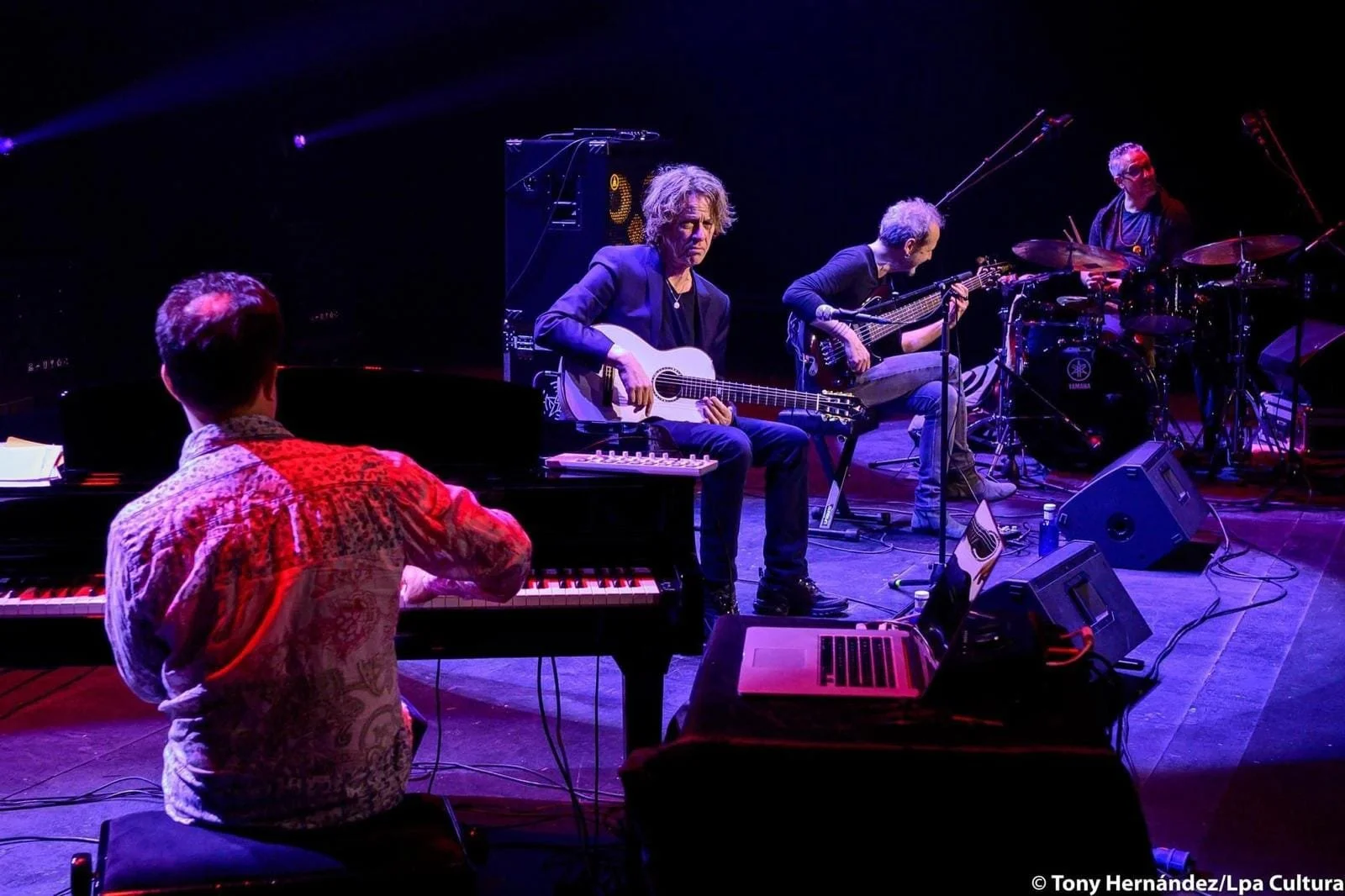 Musicians performing on stage, including a pianist, guitarist, bassist, and drummer, with stage lights and equipment.