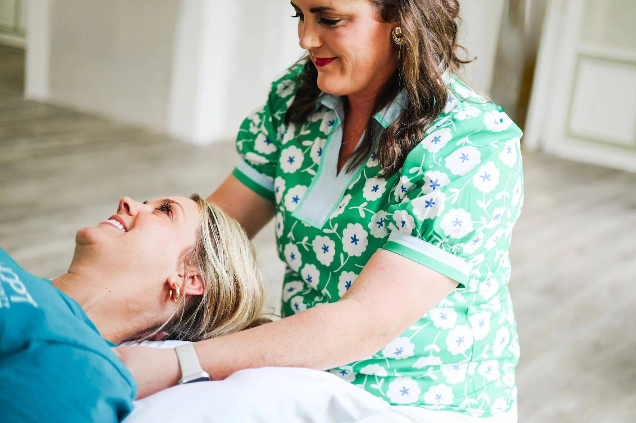 A woman in a blue shirt lying on a bed with a big smile, and Dr. Paige Riddick sitting behind her.