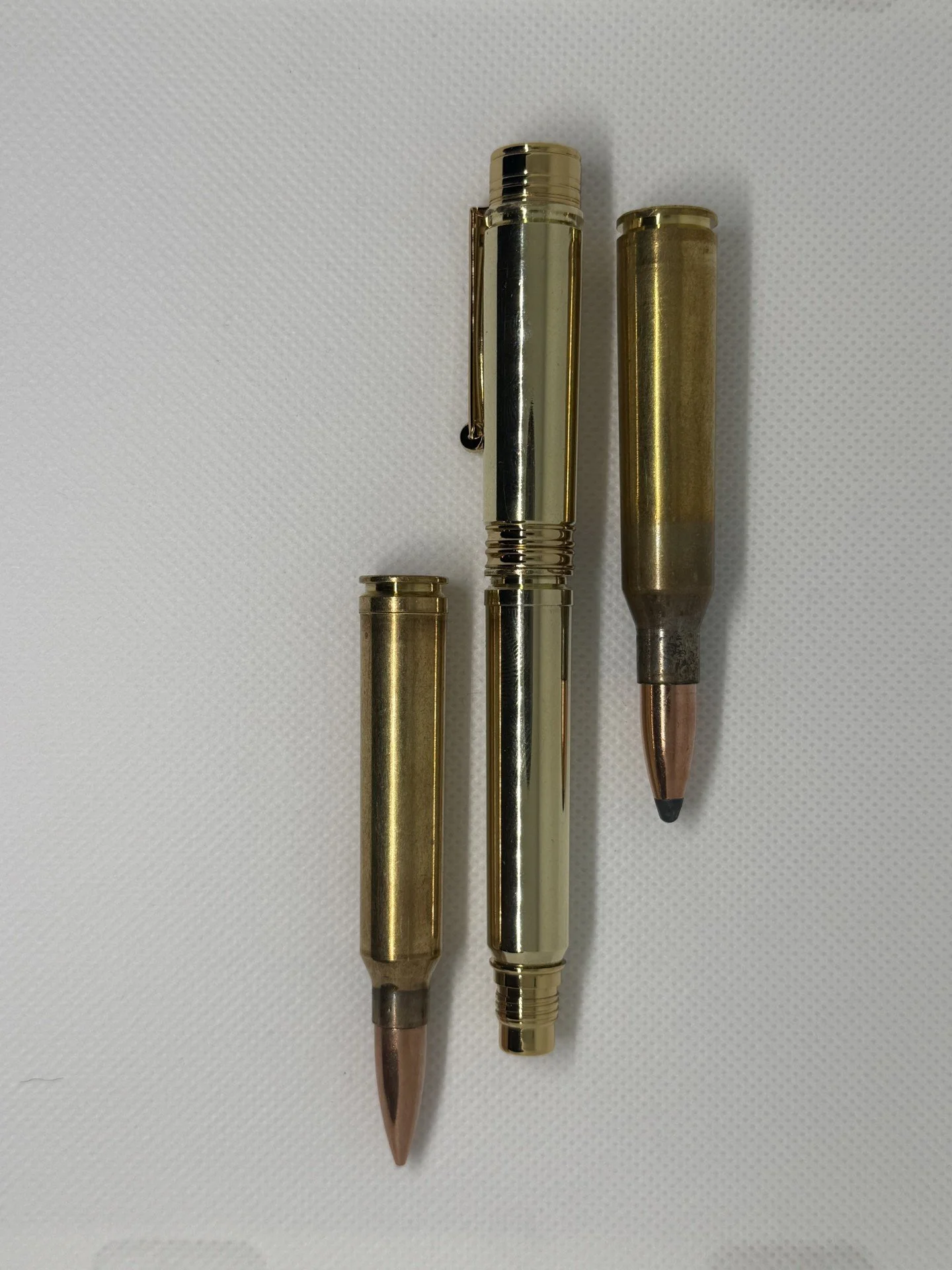 This is a fountain pen made from a .338 Lapua casing for the lid and a 300 Men for the shaft sat next to example of the rounds used to make it. 