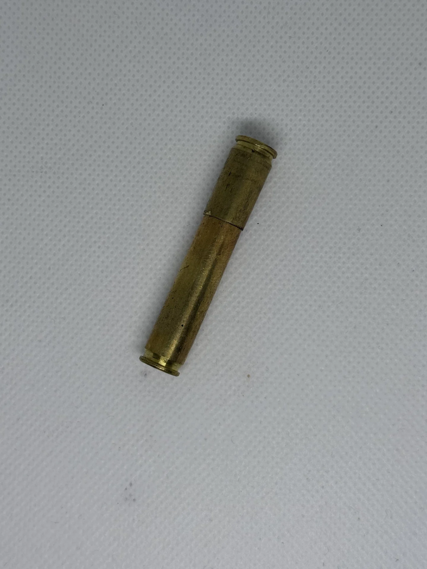 An empty brass cartridge shell lying on a white textured surface.