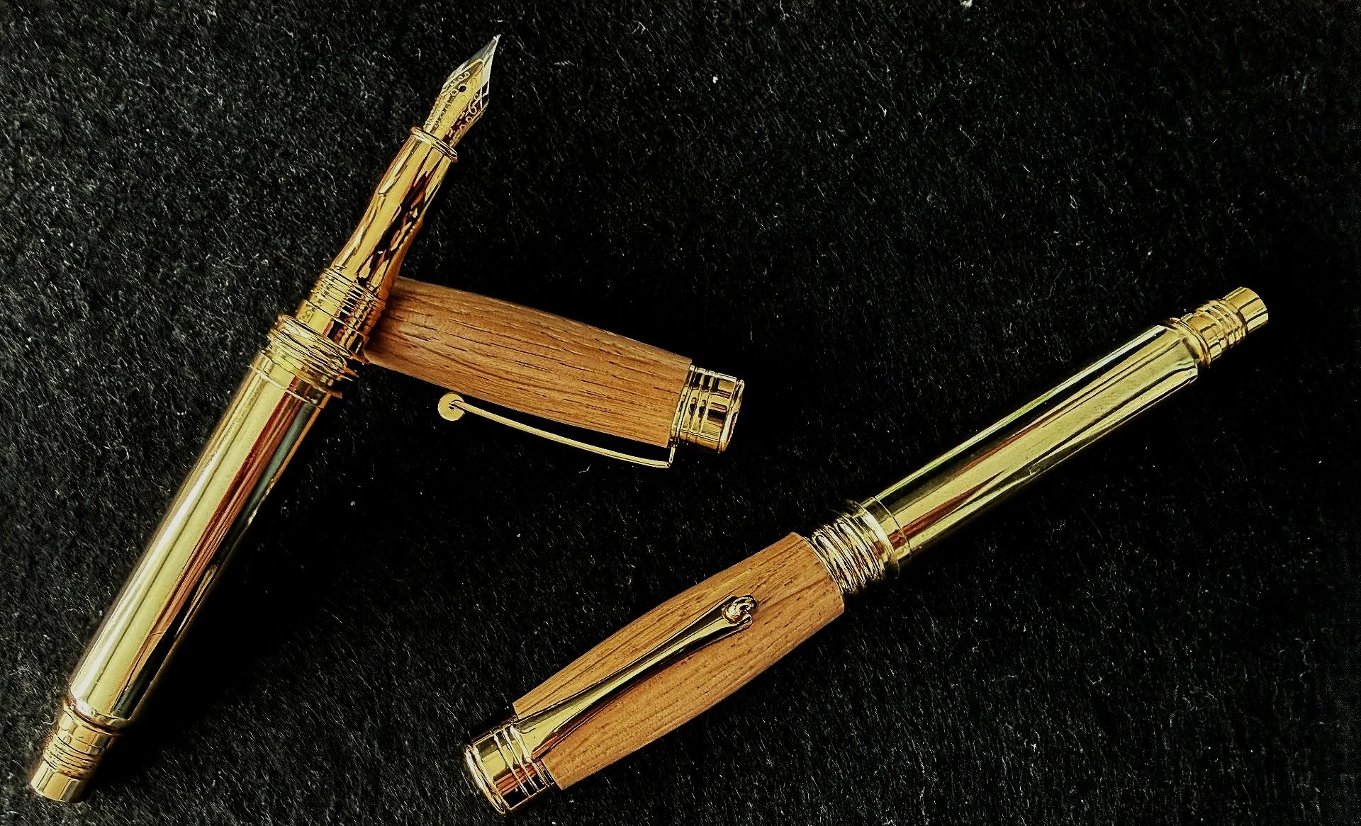 Two luxury pens with gold accents and wooden lids on a black surface.