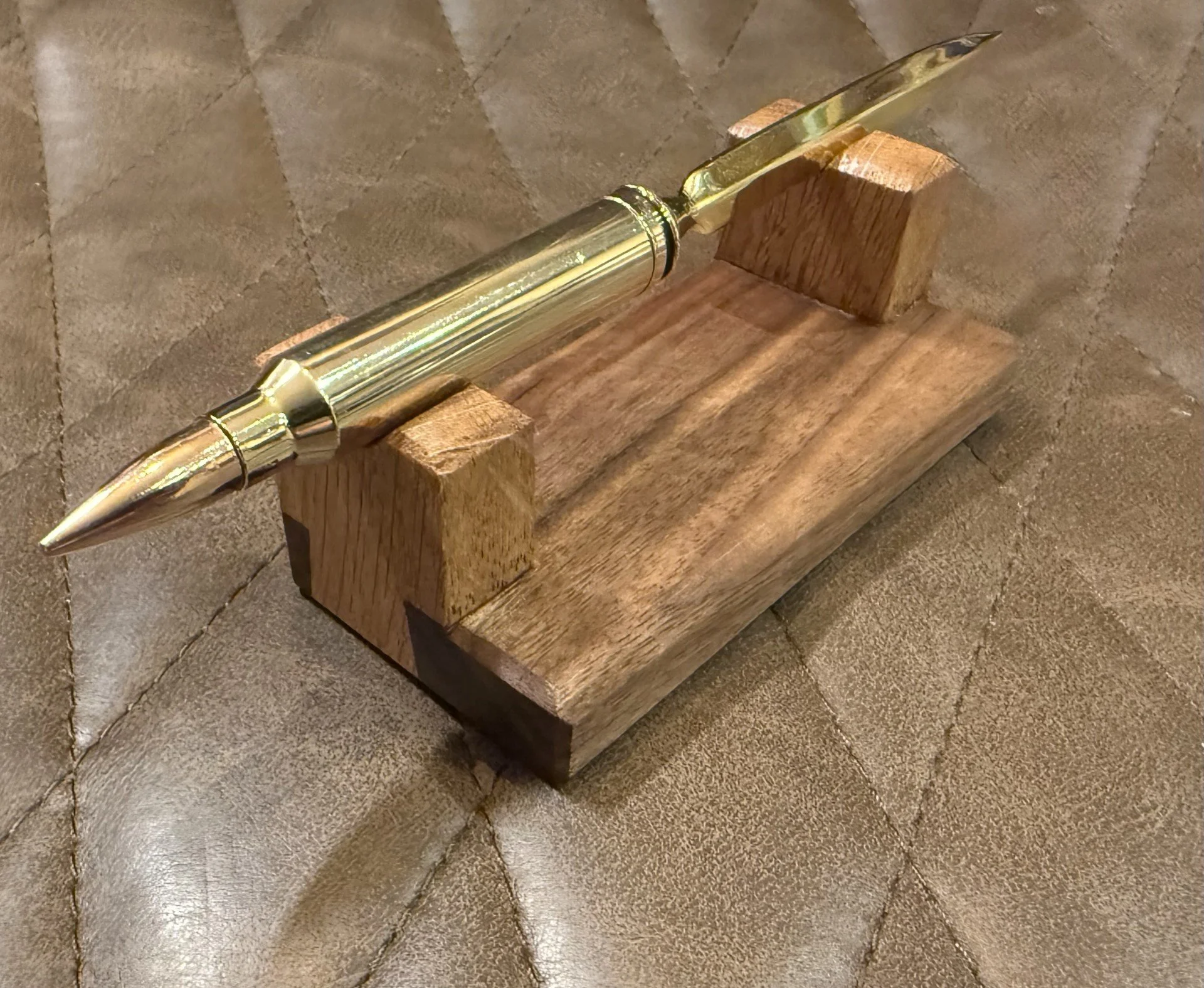 A letter opener in gold made from a once fired .300 MEN casing, with bullet replaced and a Black Walnut and White Oak hand cut dovetailed base.