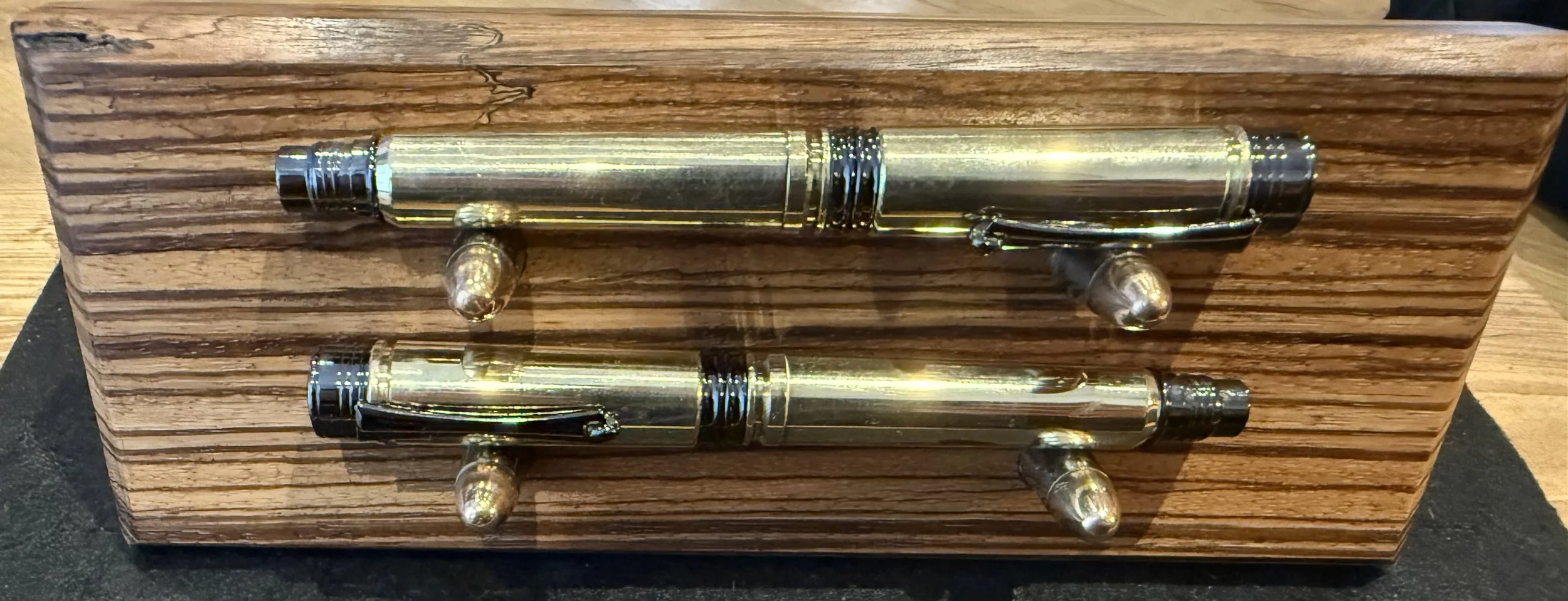 A matched set of pens.  One is a fountain pen, the other a roller ball.  Made using 300 Men casings for the shafts and 338 Lapua casings for the lids.  The stand is made from a piece of Zebrano using once fired 9mm casings and bullets for hold the pe