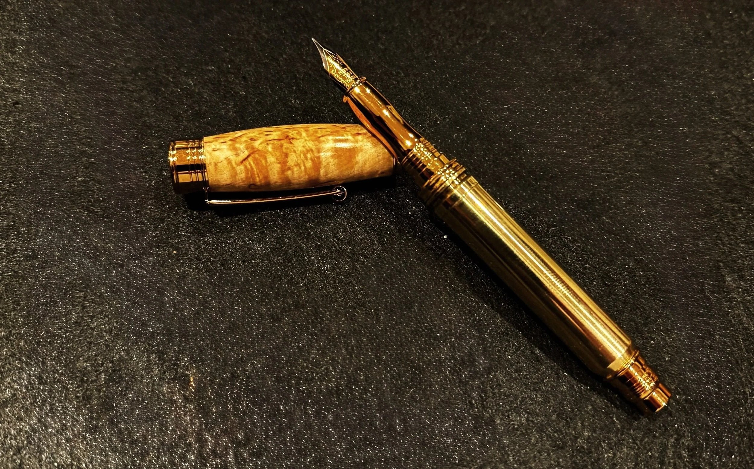 A gold-colored pen with a wooden grip resting on a black textured surface.
