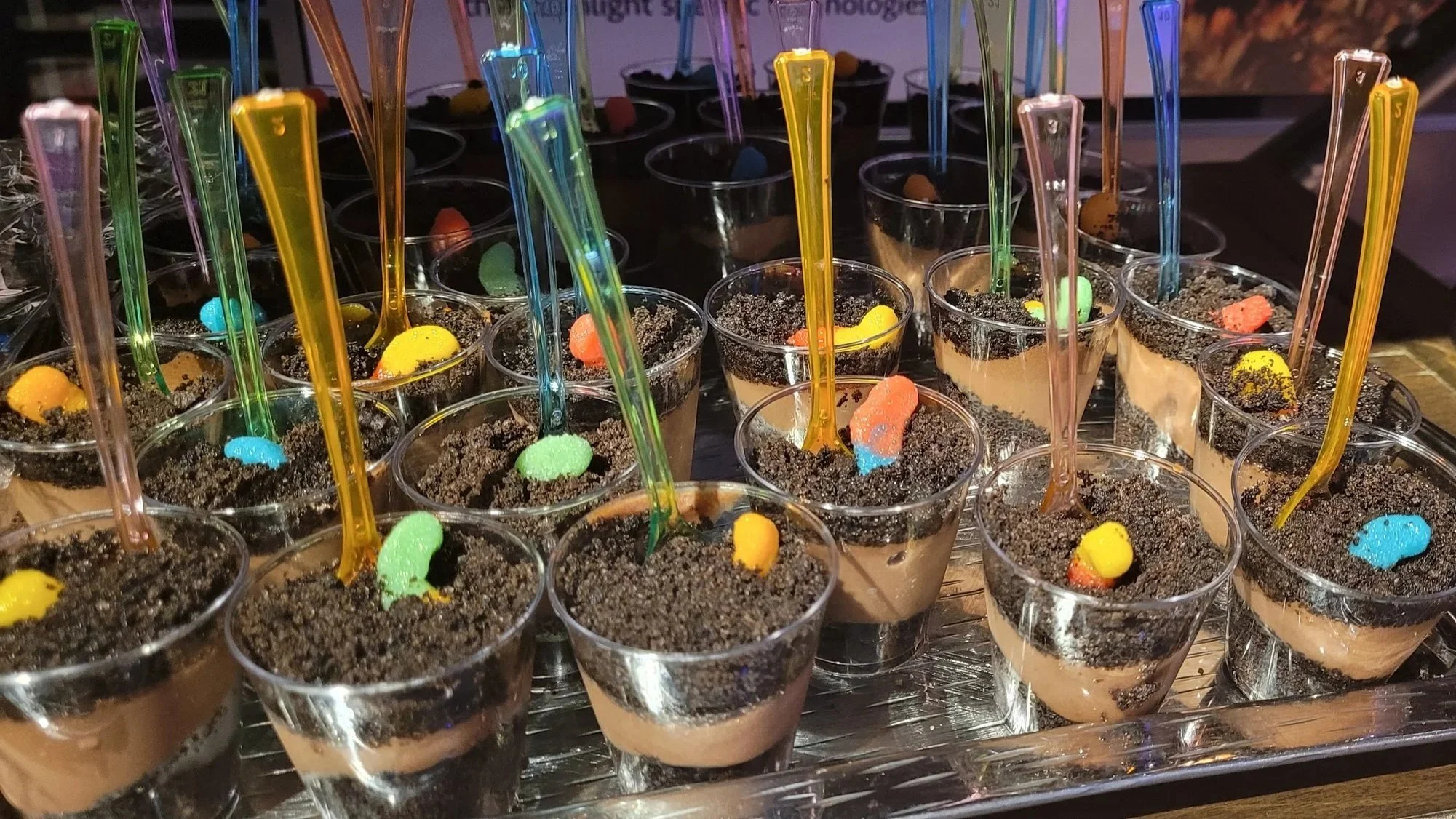 A collection of small cups filled with chocolate pudding, crushed Oreo cookies and colorful candies, each with a colorful plastic spoon inserted.