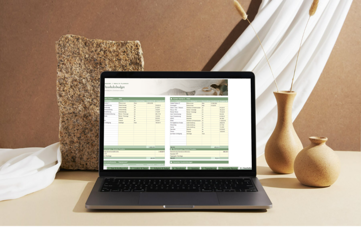 Ein Laptop zeigt eine Tabelle auf dem Bildschirm, umgeben von zwei Vasen auf einem Tisch, mit einem großen Stein und weißen Vorhängen im Hintergrund.