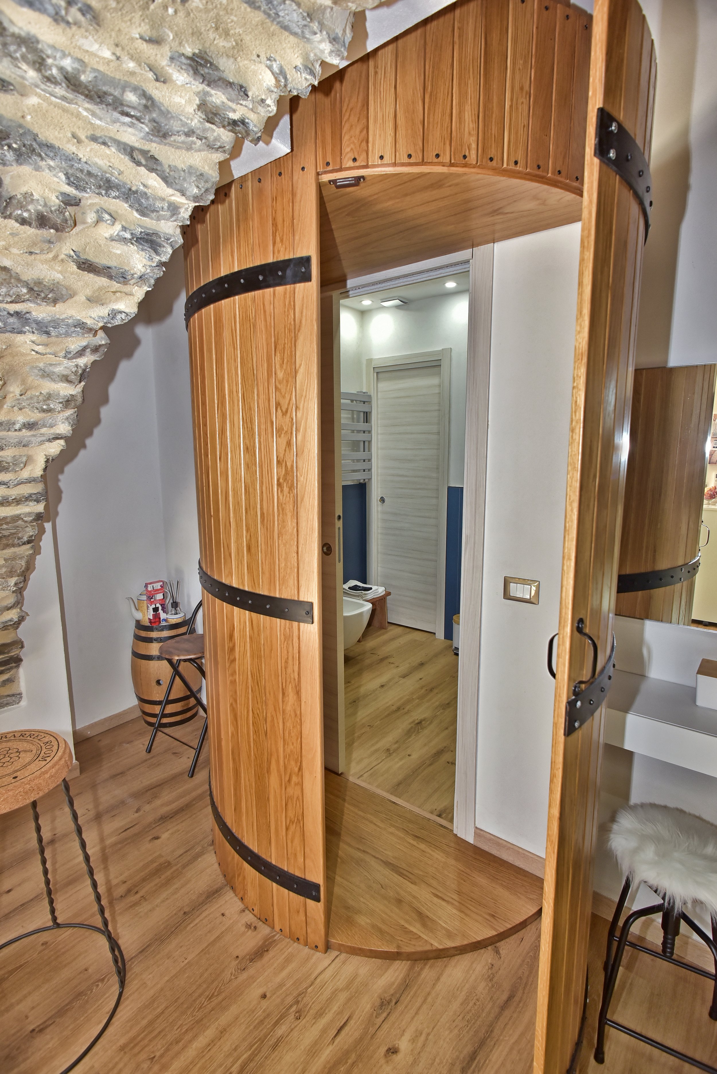 Uno specchio che riflette una stanza con pareti bianche, un armadio bianco e la porta di un bagno con pareti blu, pavimento in legno e alcuni oggetti decorativi.