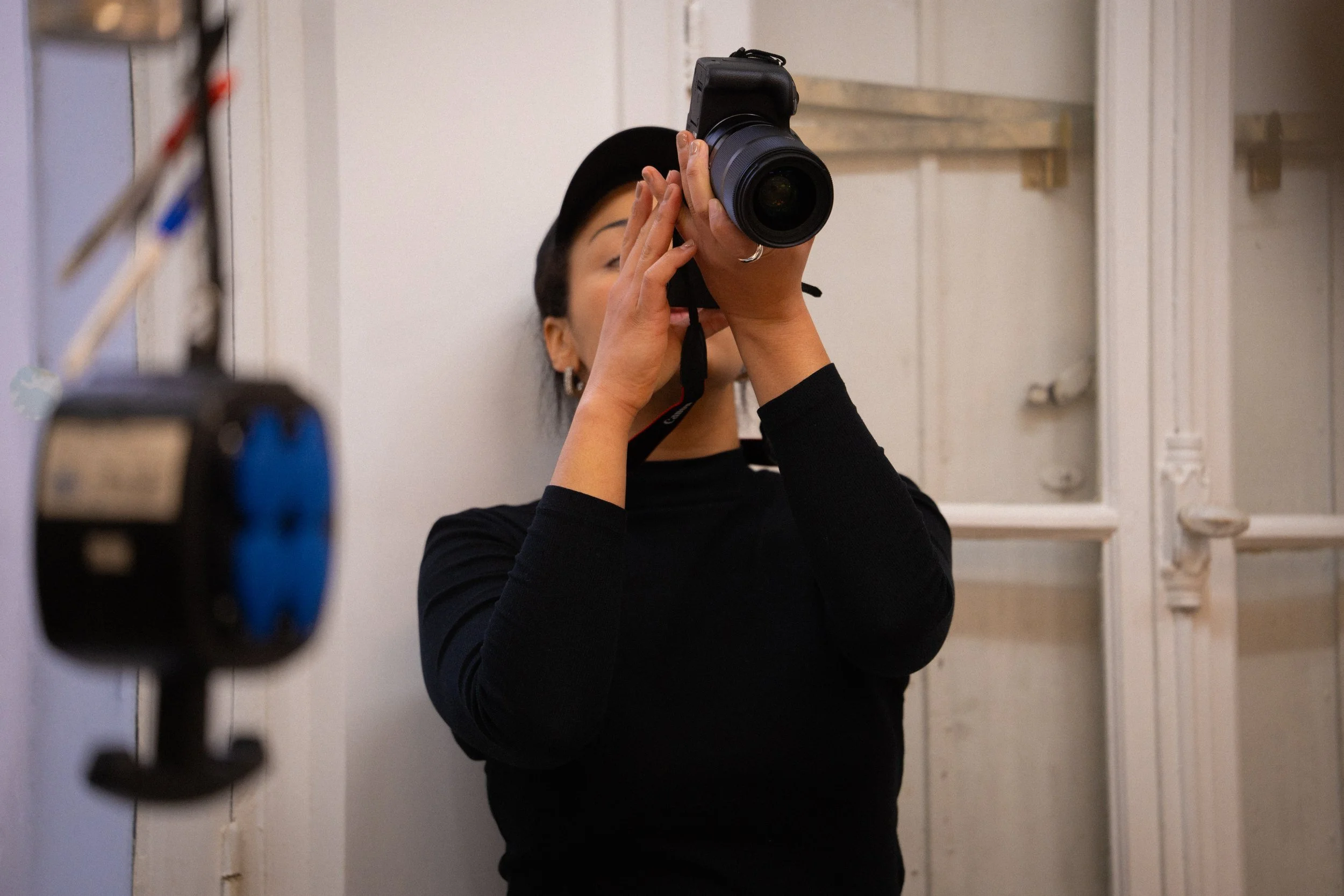 Une personne tenant un appareil photo en position de prendre une photo, avec un mur blanc en arrière-plan.