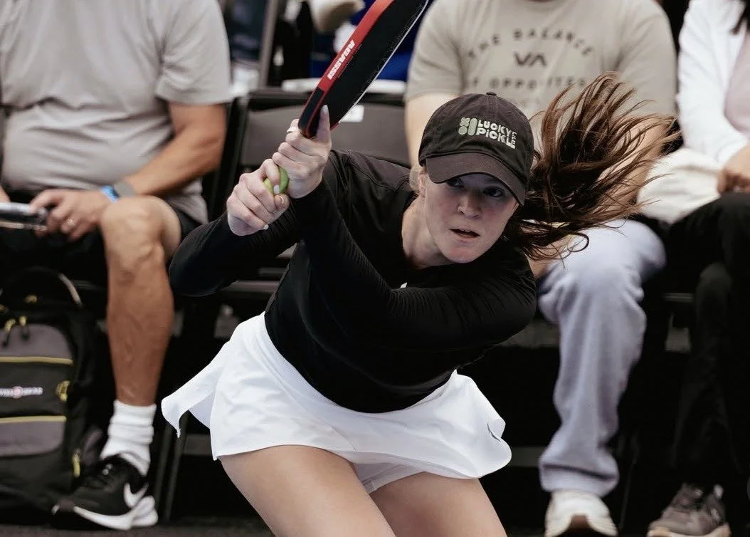 A female tennis player in motion, preparing to hit a shot during a match, with spectators in the background.
