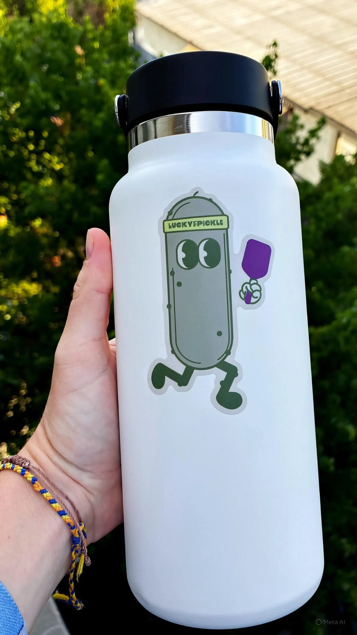 A white water bottle with a black lid and a cartoon sticker of a running pickle holding a purple ice pop, with the label 'LUCKY PICKLE'.