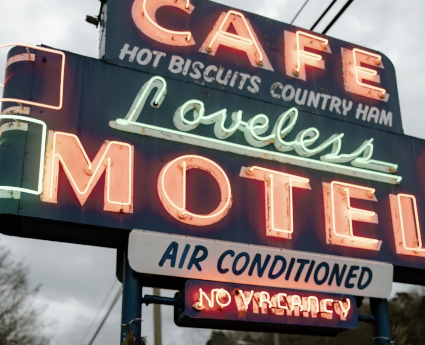 Neon sign advertising a cafe with hot biscuits, country ham, and MOTEL, also indicates air conditioned and no vacancy.