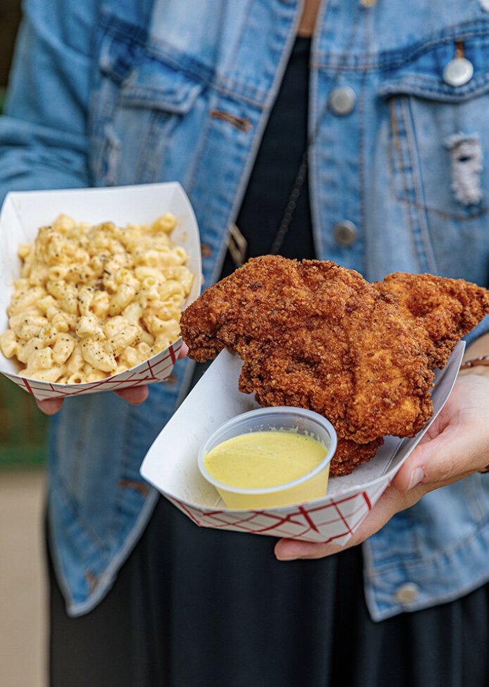 Person holding a tray with fried chicken, a cup of dipping sauce, and a side of macaroni and cheese.