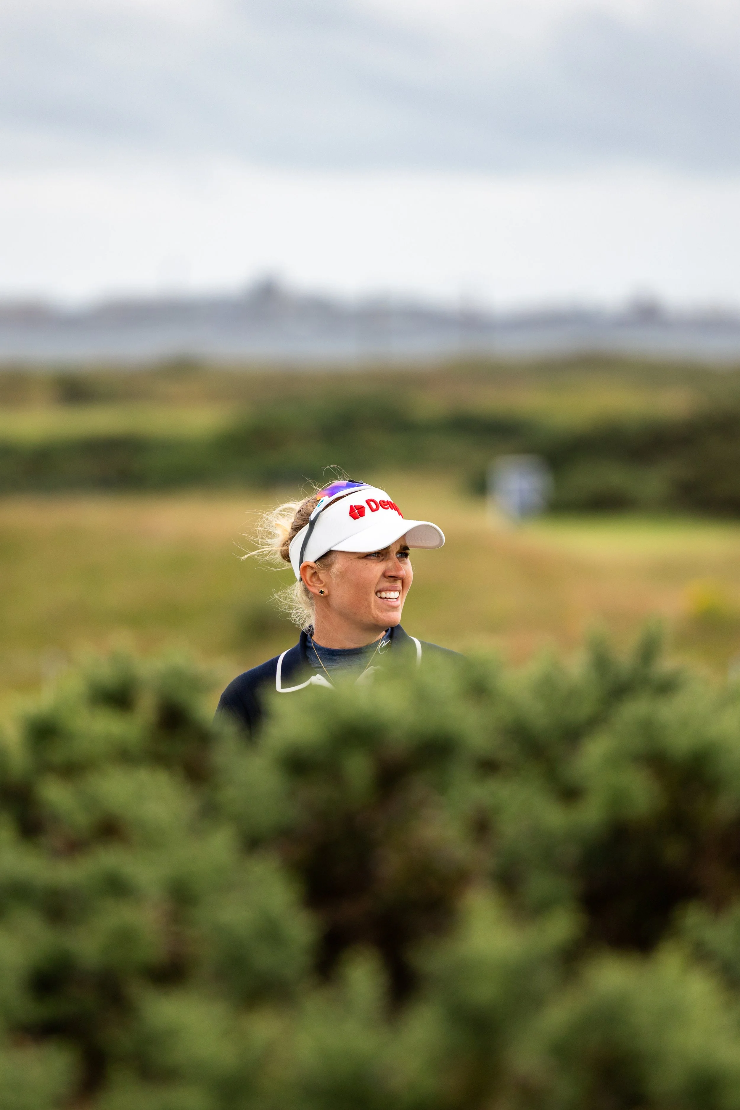 A woman wearing a white visor hat and sportswear is smiling outdoors in a green field with blurred background.