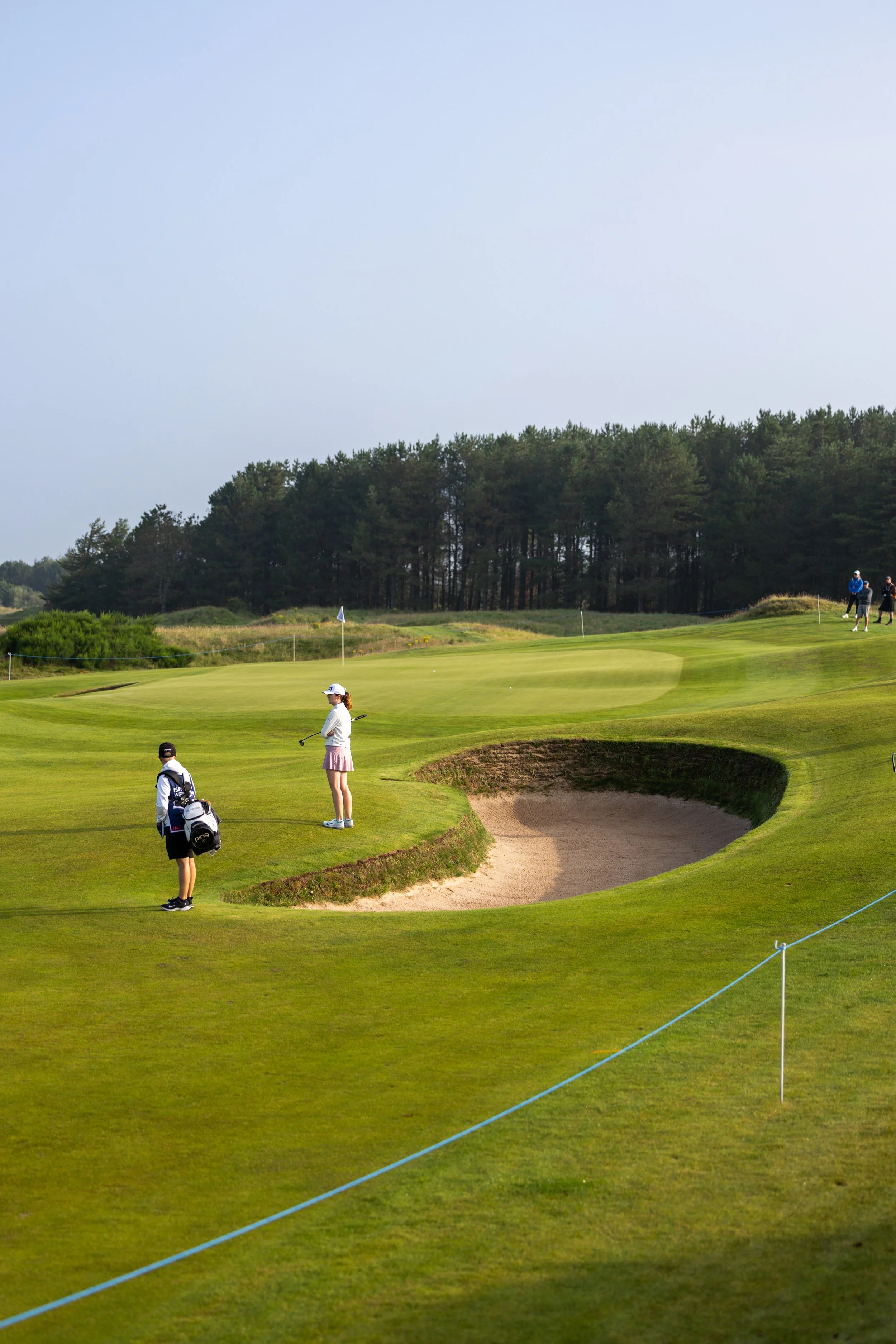 Golf course with players, sand trap, and trees in the background