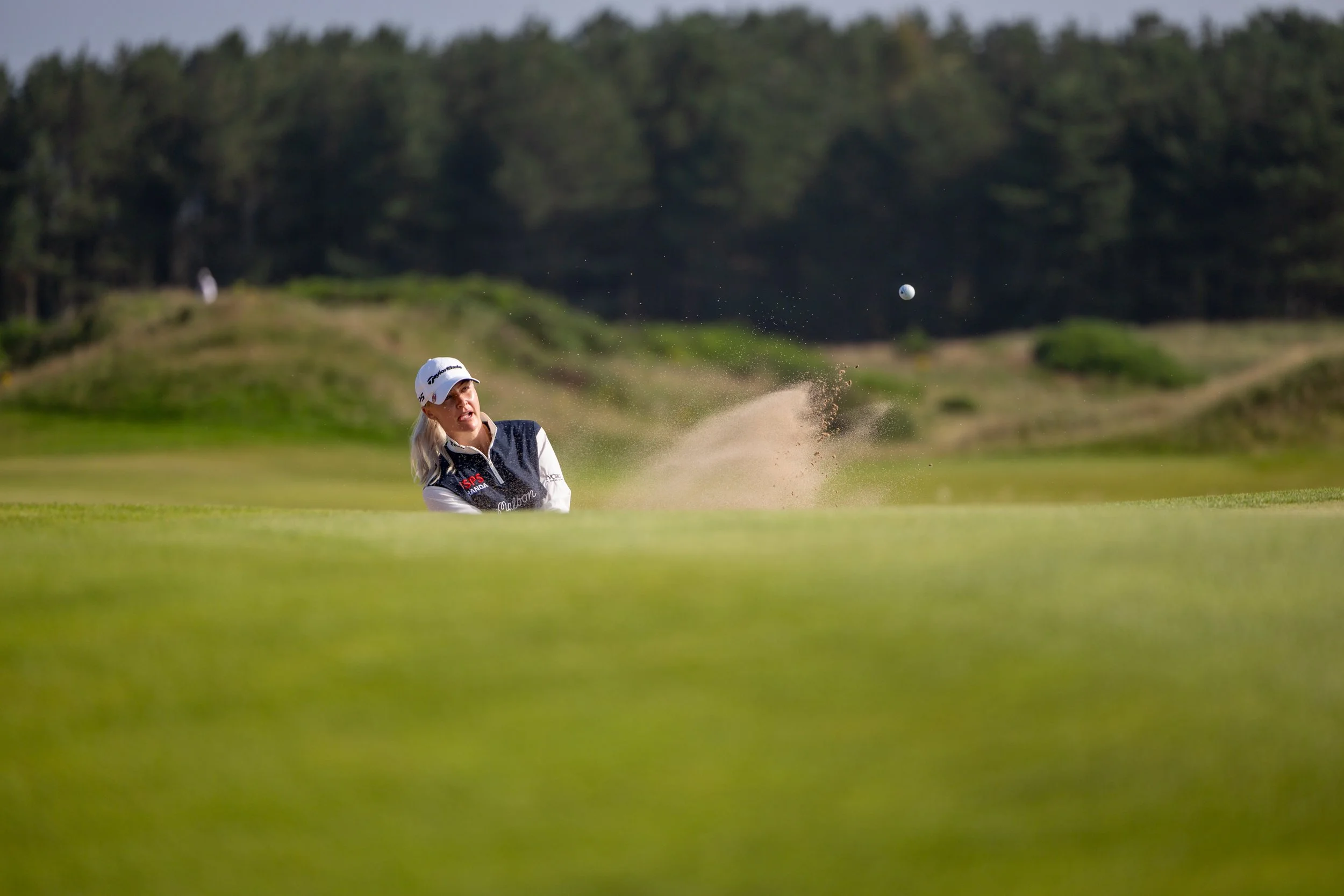 A female golfer hitting a shot from a sand trap on a golf course during daytime.