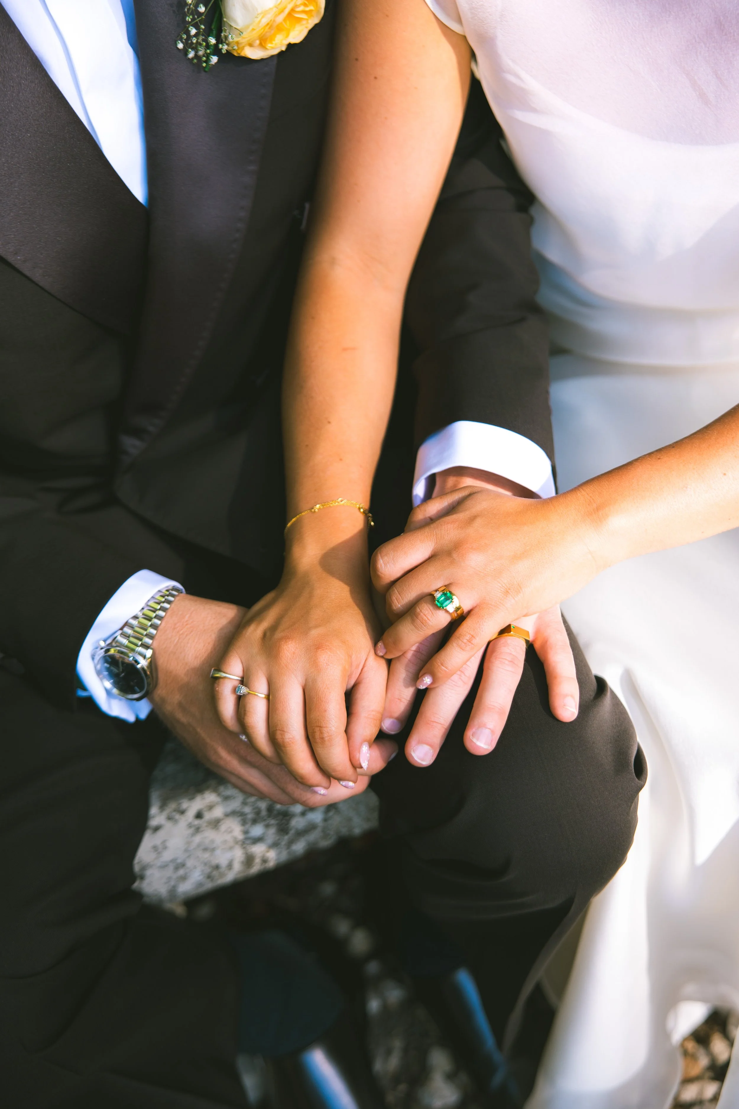 Close-up of hands stacking in a sign of unity, with people dressed in formal attire, including suits and rings, suggesting a celebration or ceremony.