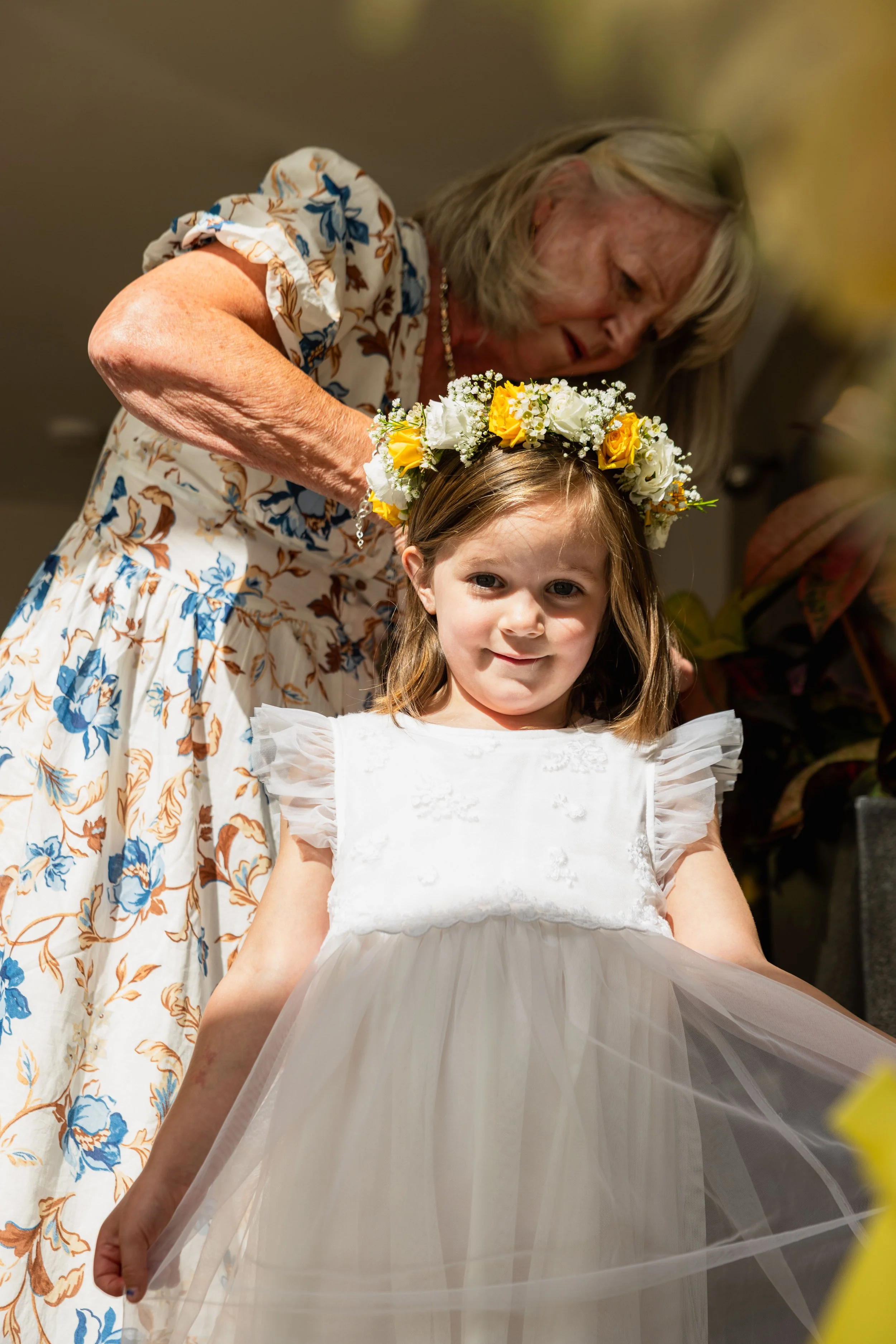 An elderly woman placing a flower crown on a young girl's head during a special celebration or ceremony.