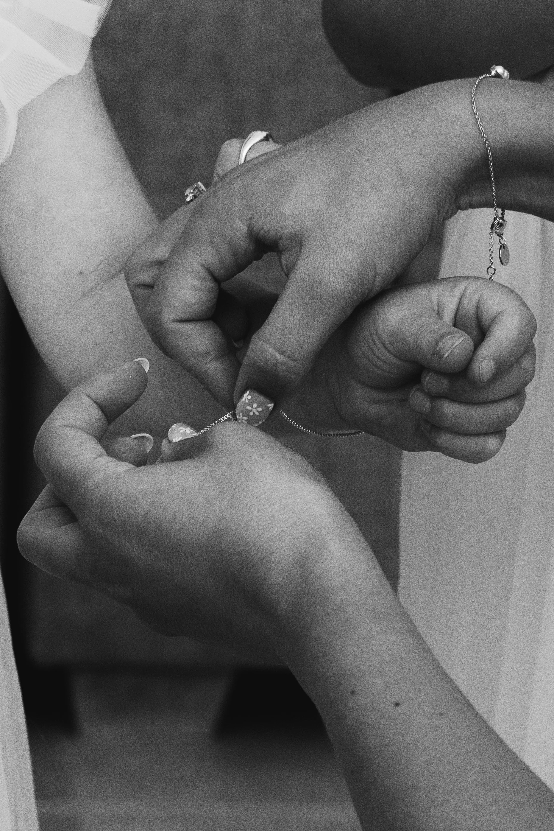 Two hands, one with a ring and the other with a bracelet, are holding a chain.