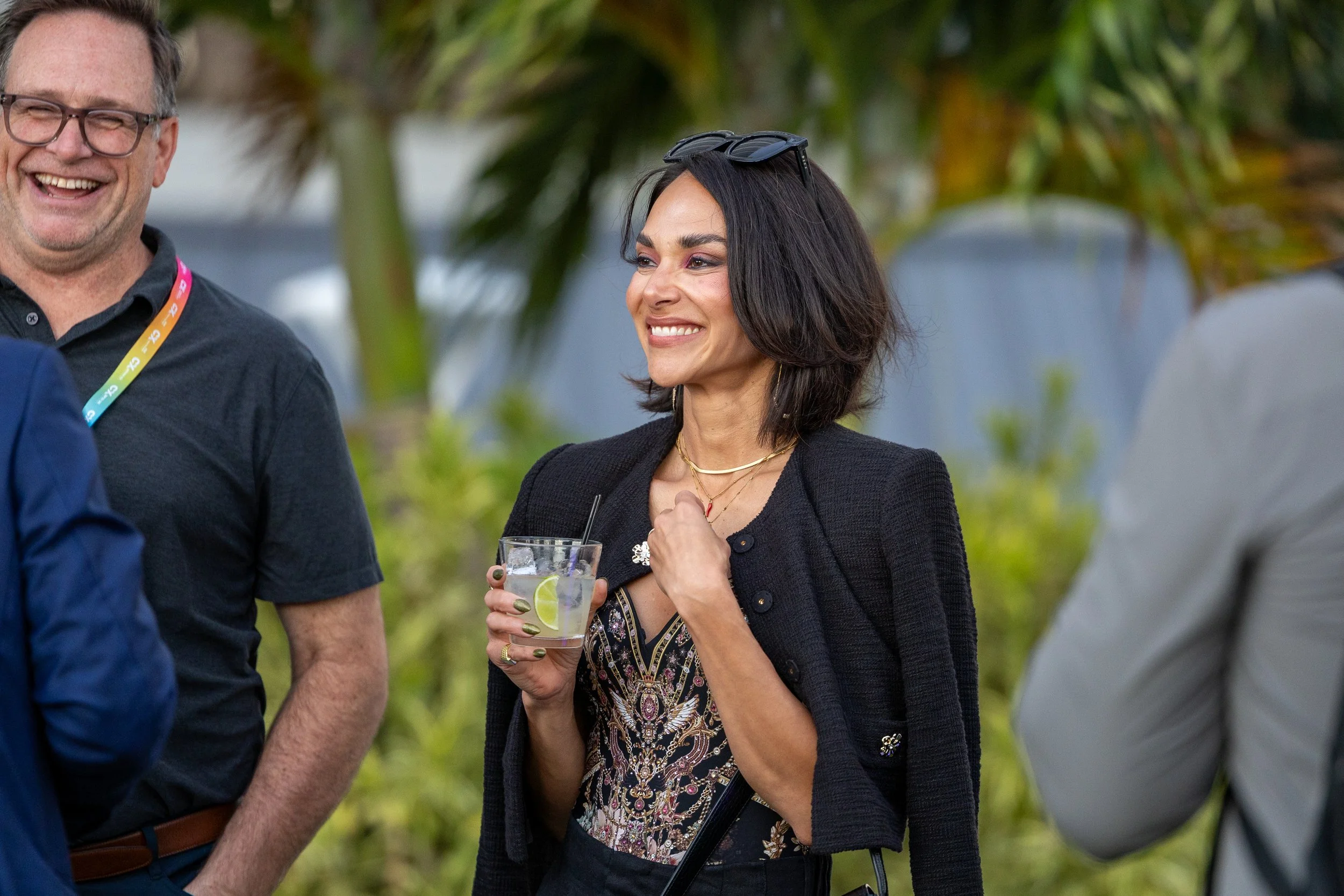 A woman with dark hair holding a glass with lemon slices, standing outdoors at a social gathering.