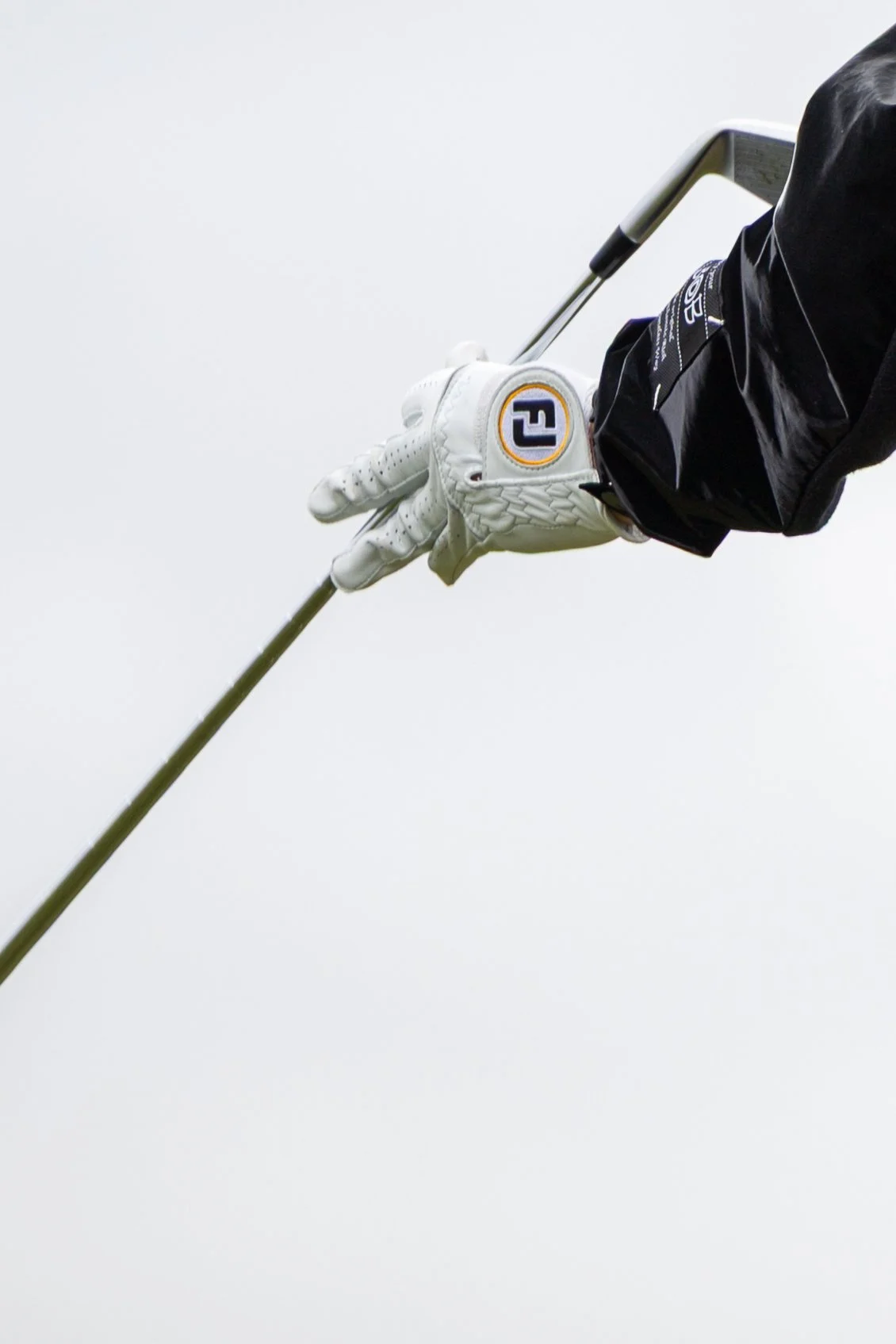 Close-up of a golfer's hand in a white glove gripping a golf club against a blank sky background.