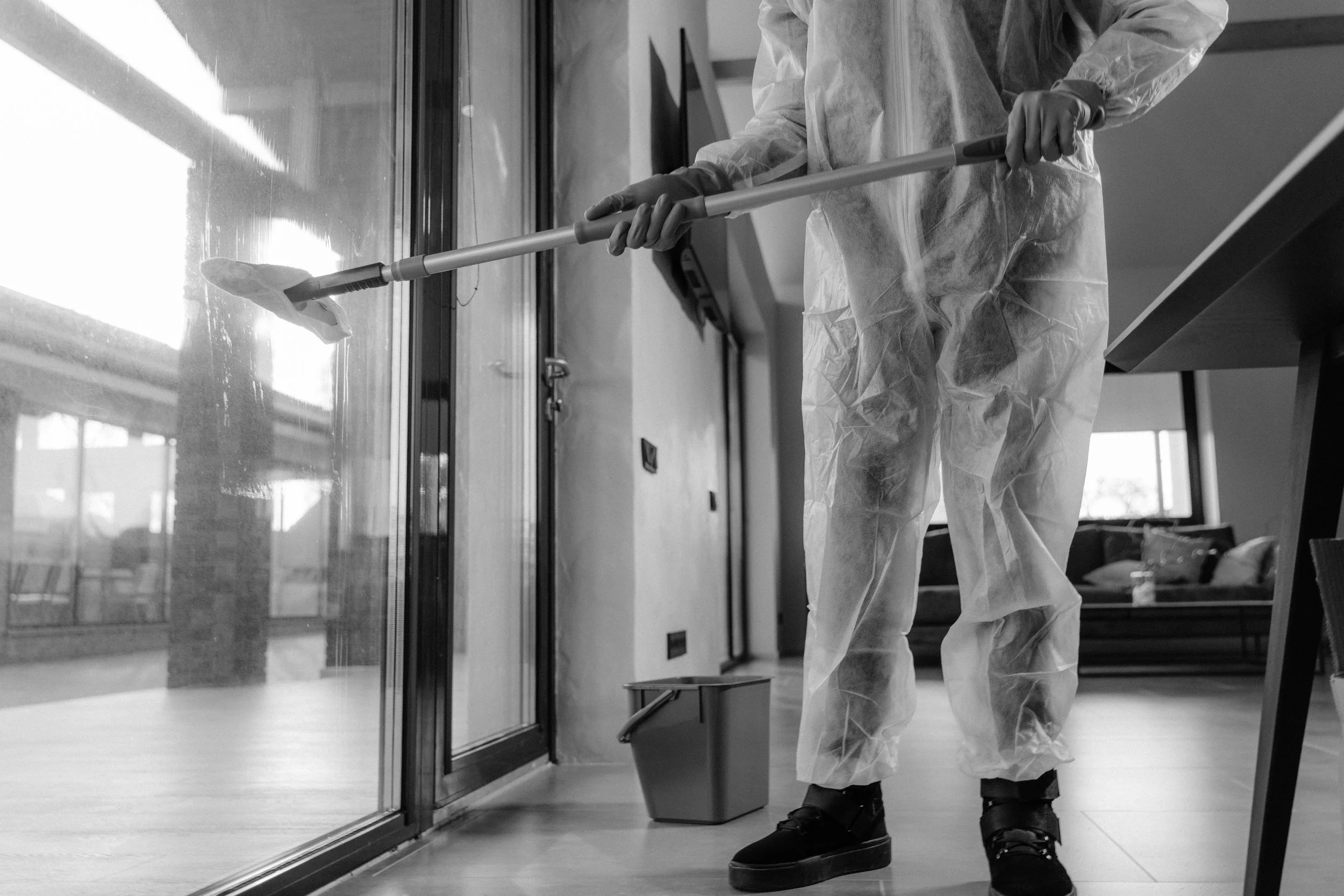 Person wearing protective gear cleaning a glass door with a mop in an indoor setting.