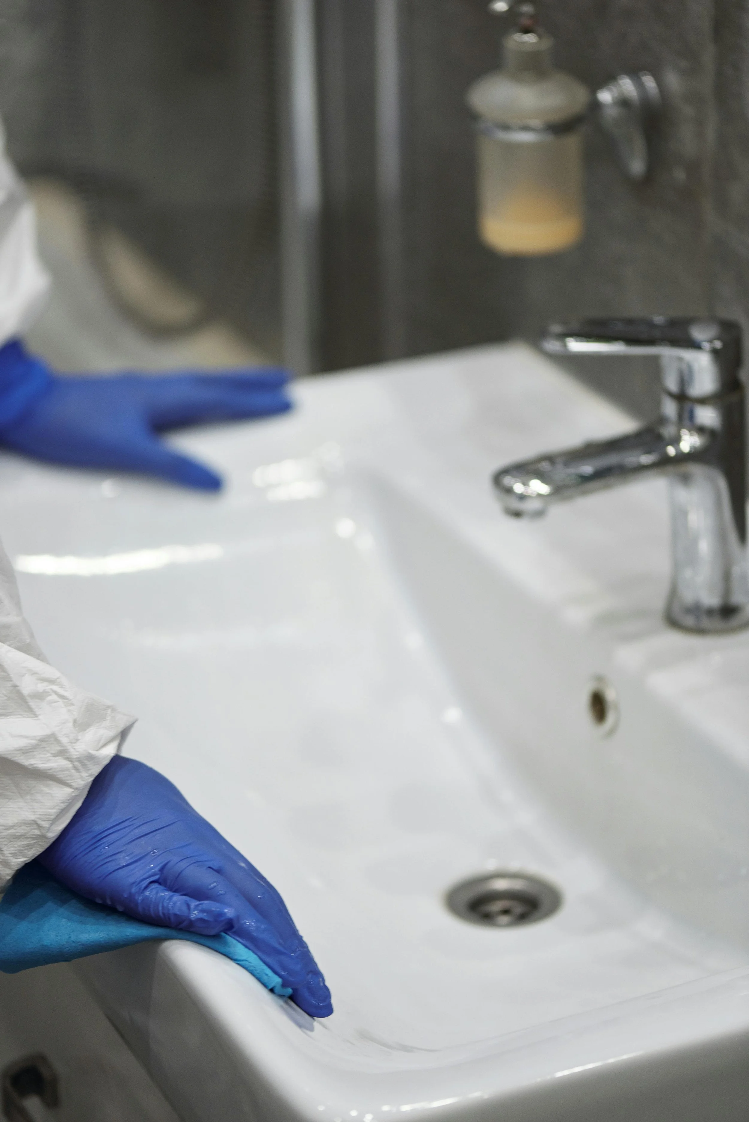 Close-up of a person wearing blue gloves cleaning a white sink.