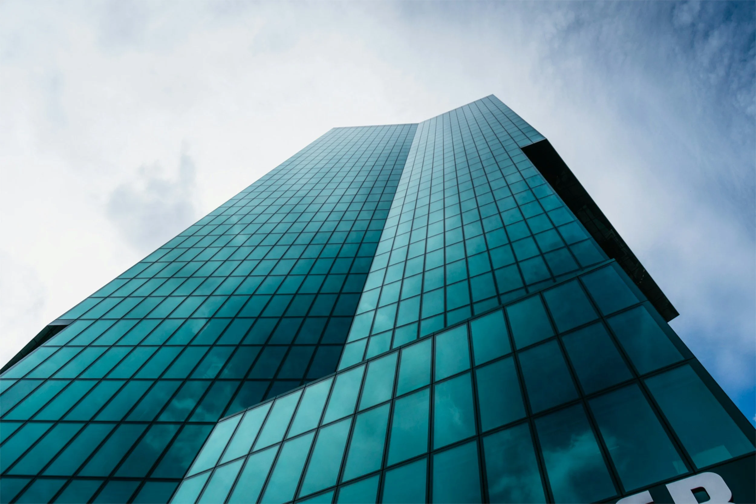Low-angle view of a tall, modern glass skyscraper against a cloudy sky.
