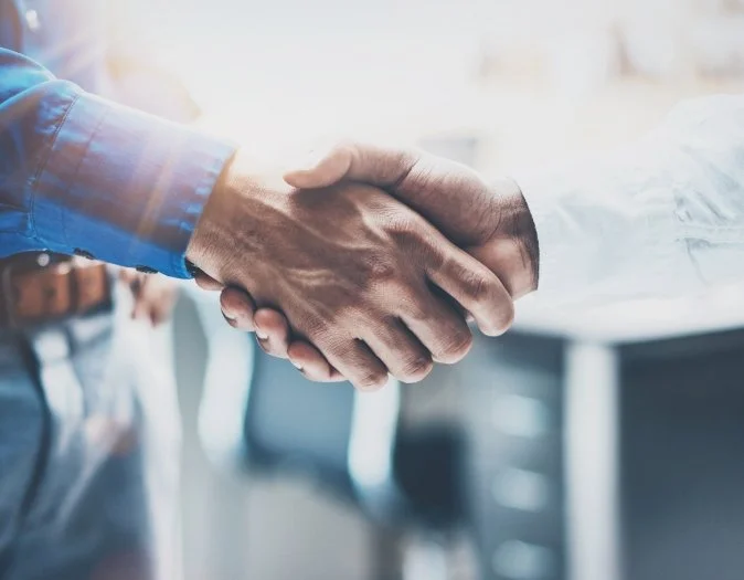 Close-up of two people shaking hands in a well-lit office setting.