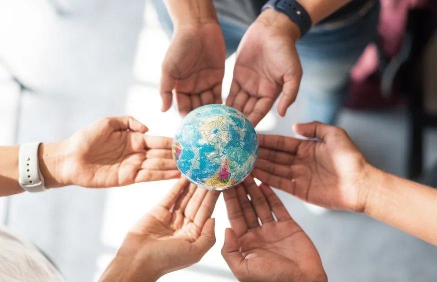 Multiple hands holding a small globe of Earth together, symbolizing unity and global cooperation.