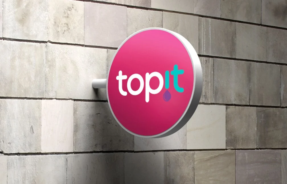 A round pink and gray sign for "toppit" mounted on a beige stone wall.