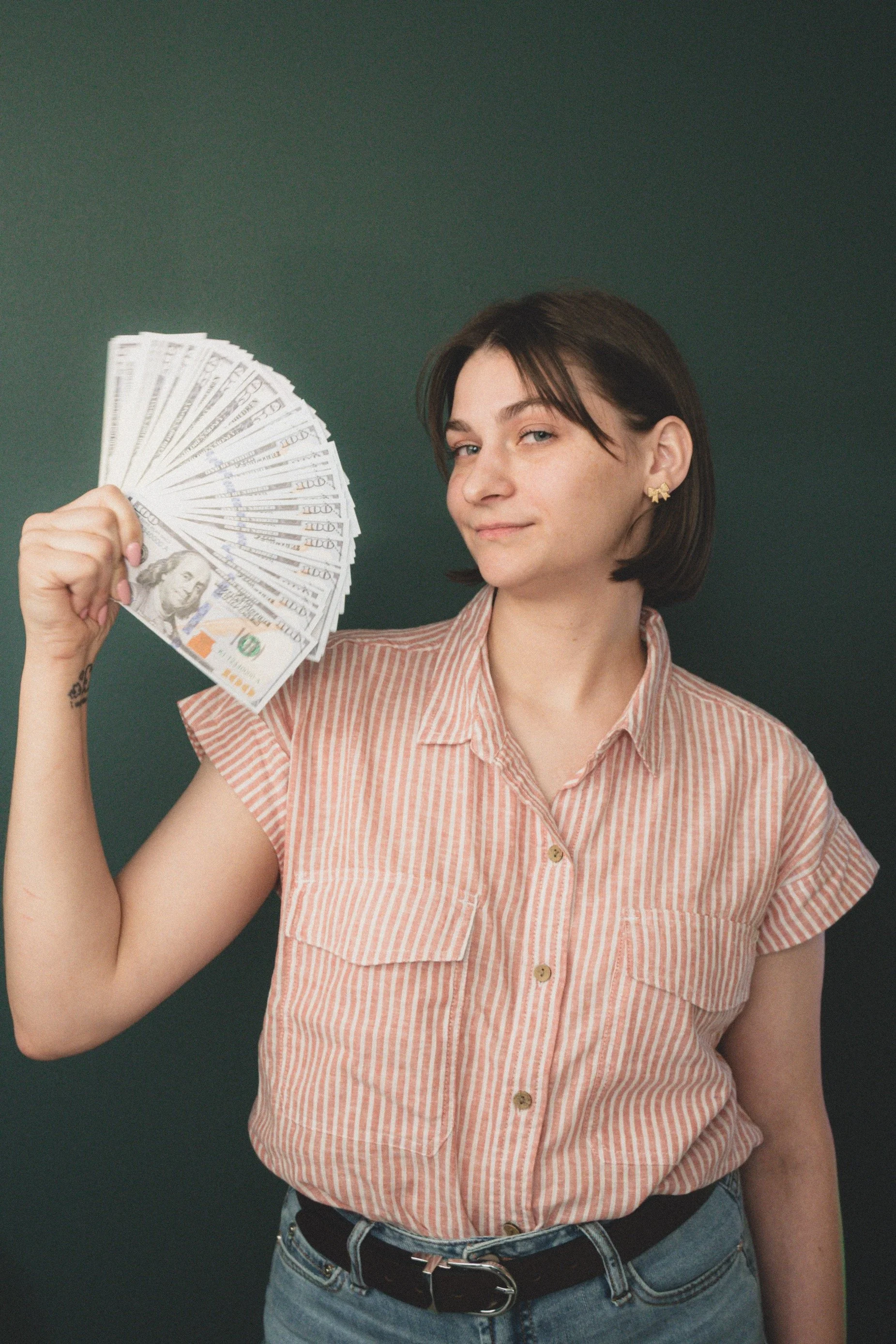 Dria Benjamin, host of the Have You Tried Being Rich podcast, holding a fan of $100 bills during a promotional photoshoot about personal finance and wealth-building.