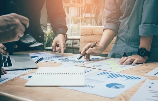 People working on a business project with documents and charts on a wooden table.