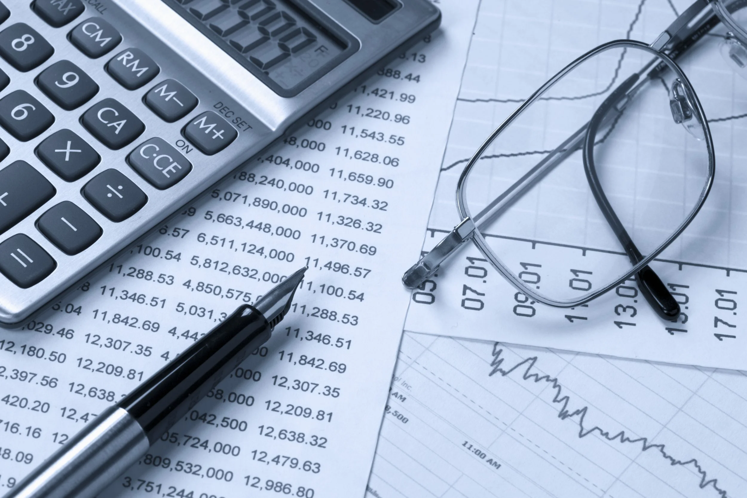 A calculator, a pair of glasses, a pen, and financial documents with charts and numerical data on a desk.